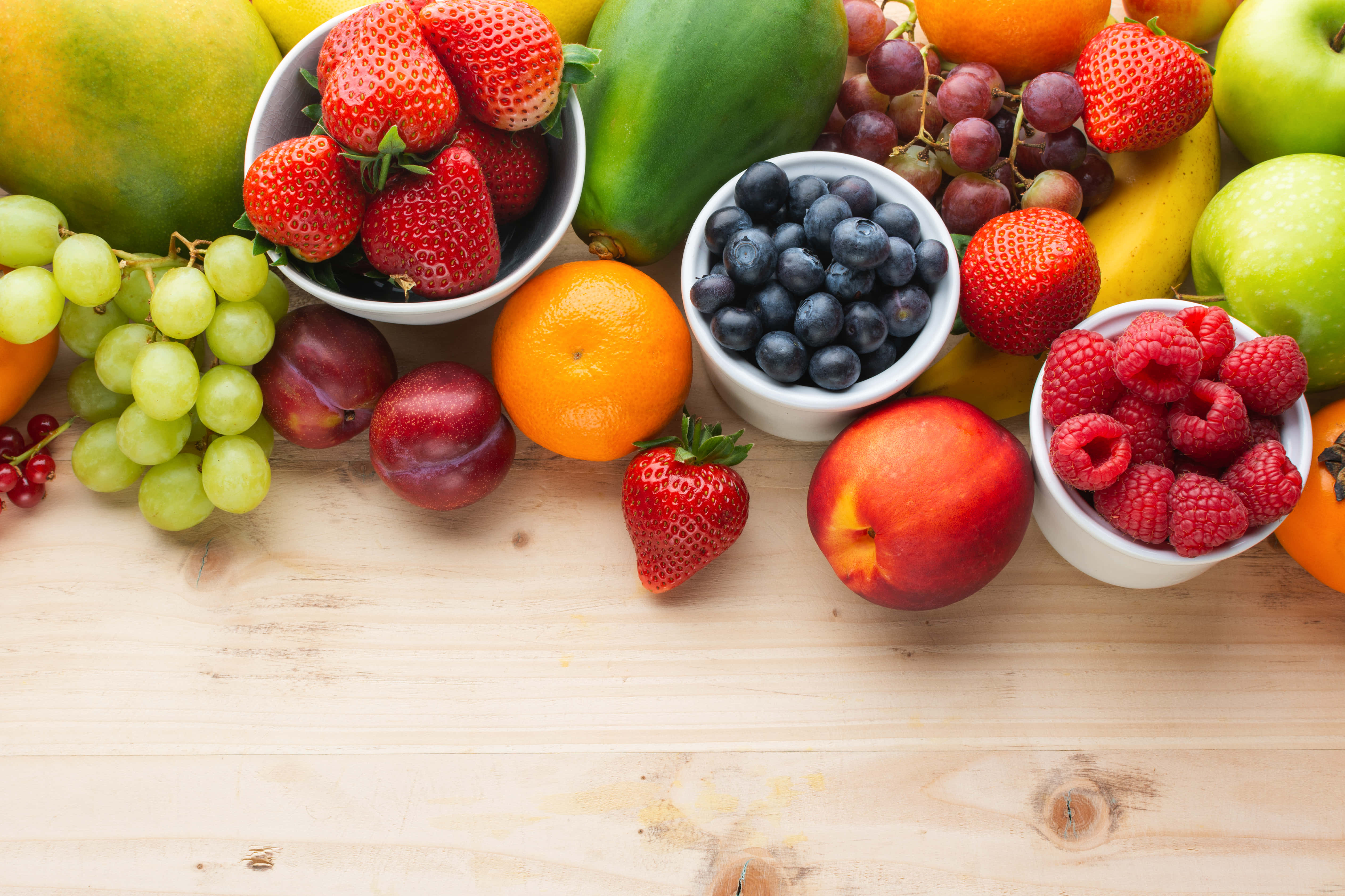 Fruit 桌布 壁紙 — 一張充滿活力的俯拍照片，展示各種新鮮水果如草莓、藍莓和覆盆子，排列在淺色木質表面上。