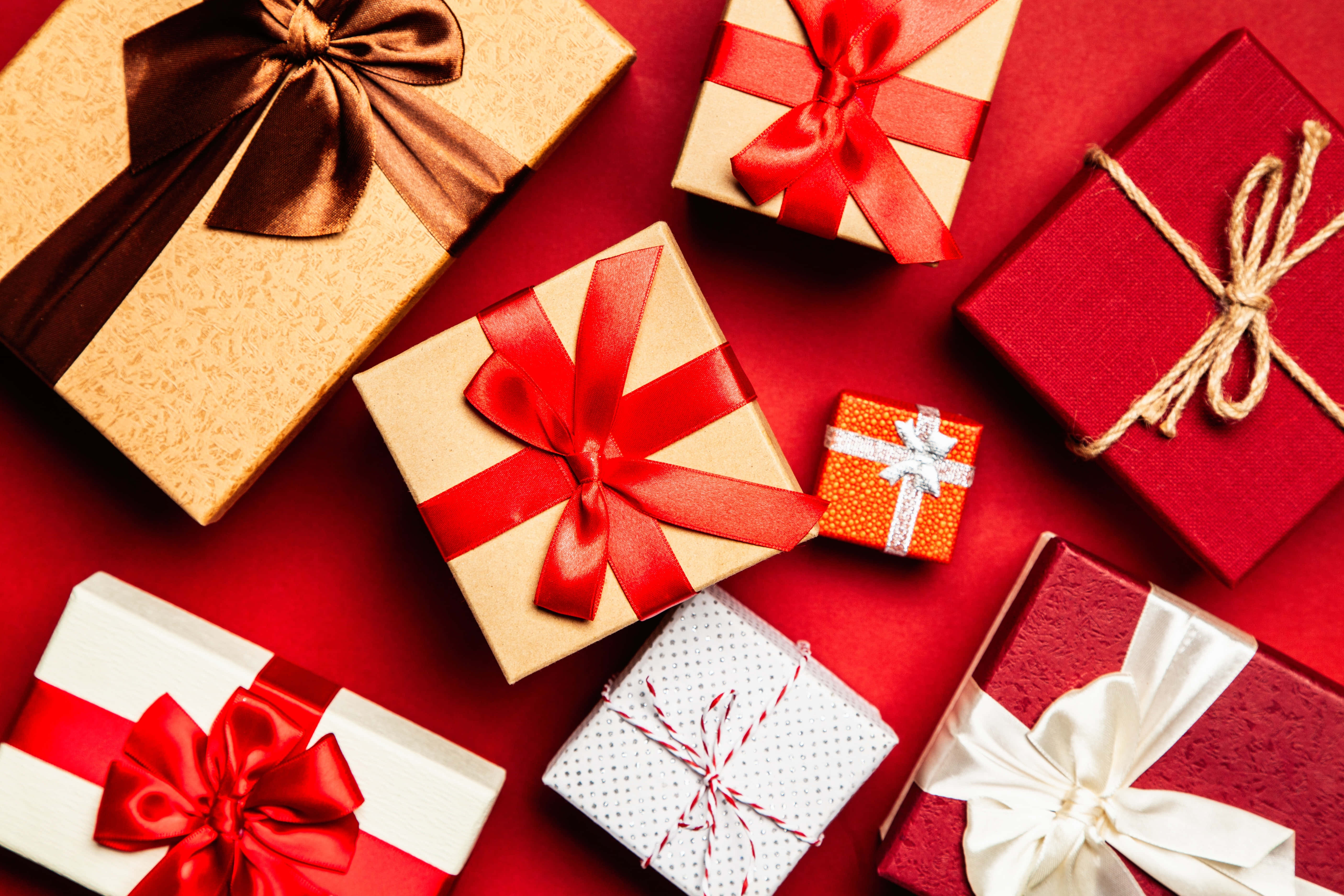 Gift 桌布 壁紙 — 一張充滿活力的俯拍照片，展示各種帶有紅色、金色和白色蝴蝶結的禮物盒，背景為大膽的紅色。