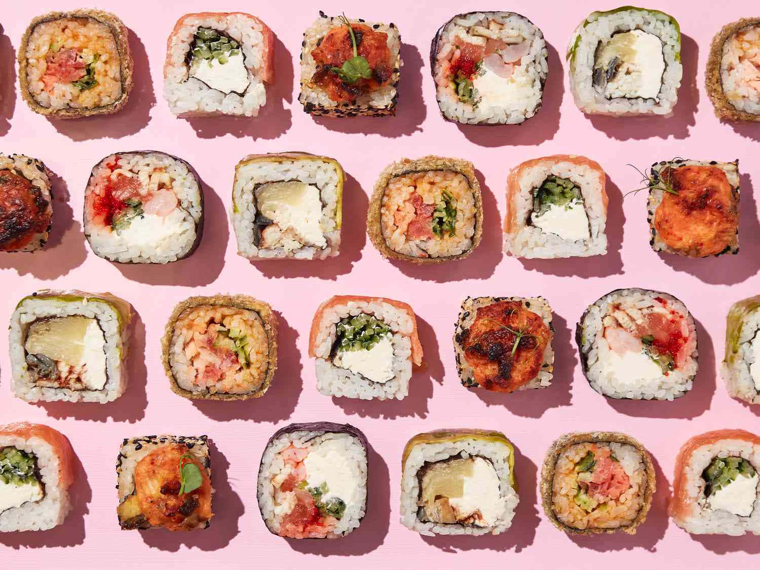 Sushi 桌布 壁紙 — 一張充滿活力的俯拍照片，展示各種壽司卷整齊排列在亮粉紅色背景上。