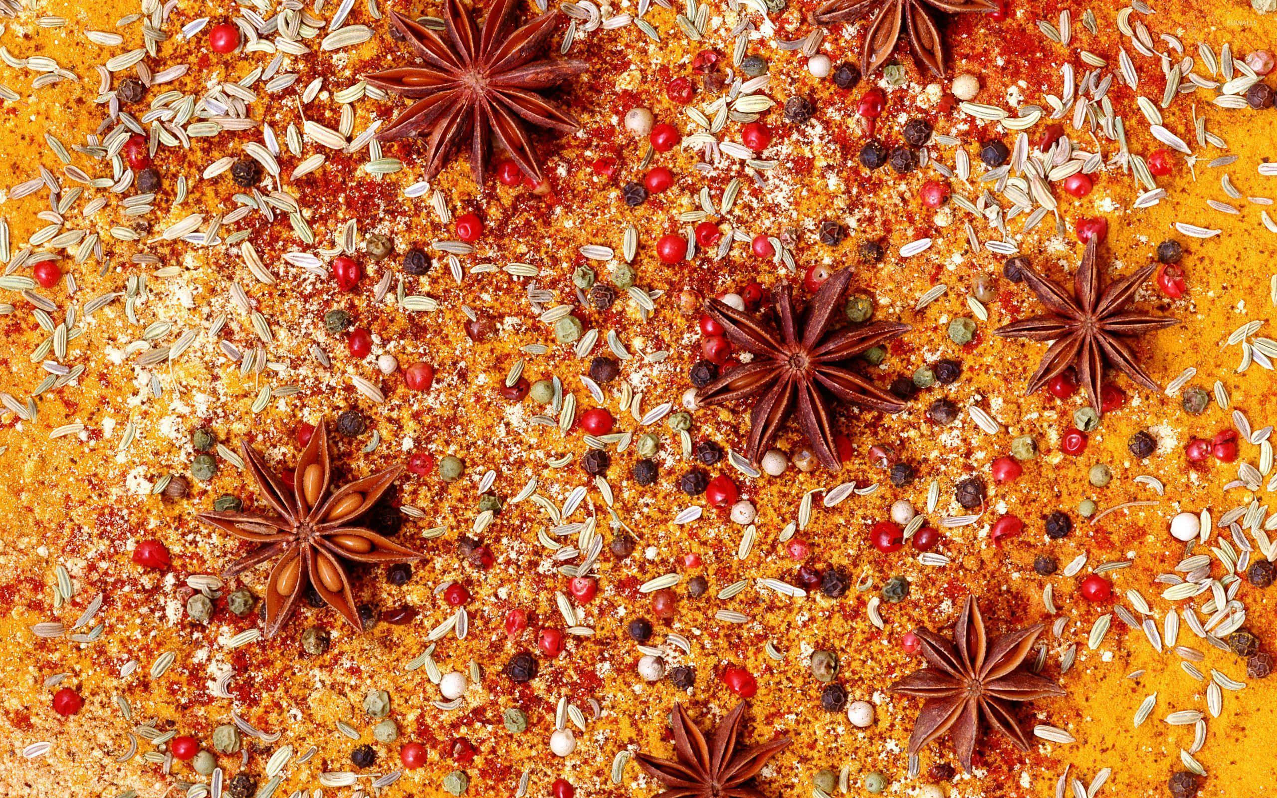 Spices 桌布 壁紙 — 一張充滿活力的俯拍照片，展示散落在溫暖橙色香料床上的八角、胡椒粒和種子。