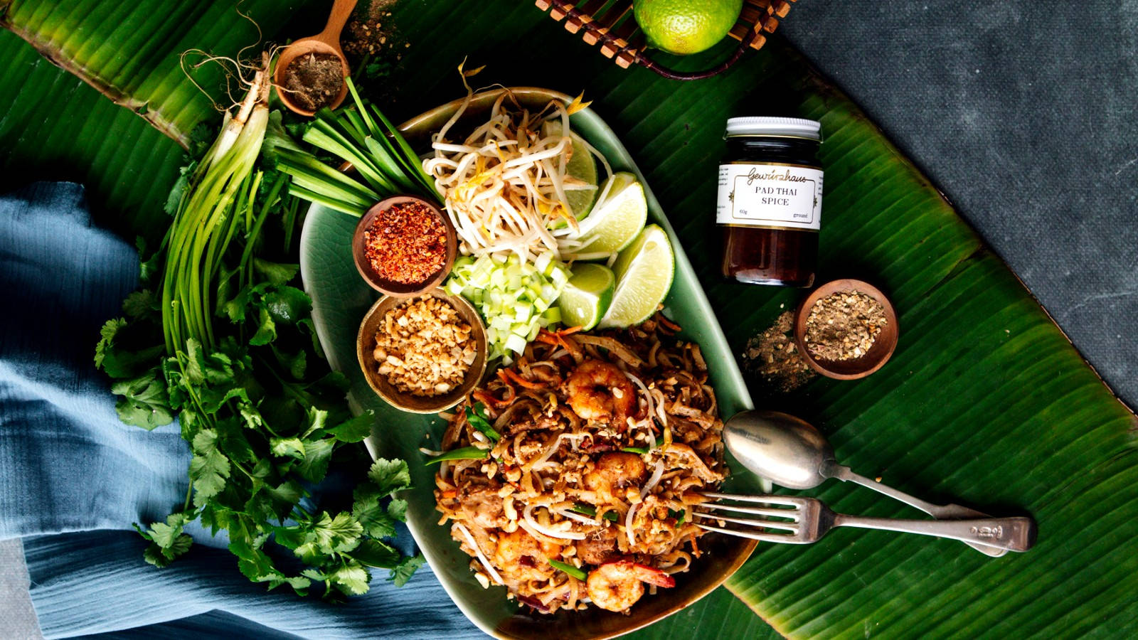 thai 桌布 壁紙 — 一張充滿活力的俯拍照片，展示香蕉葉上的泰式炒河粉配蝦仁，並以豆芽、青檸和香草點綴。
