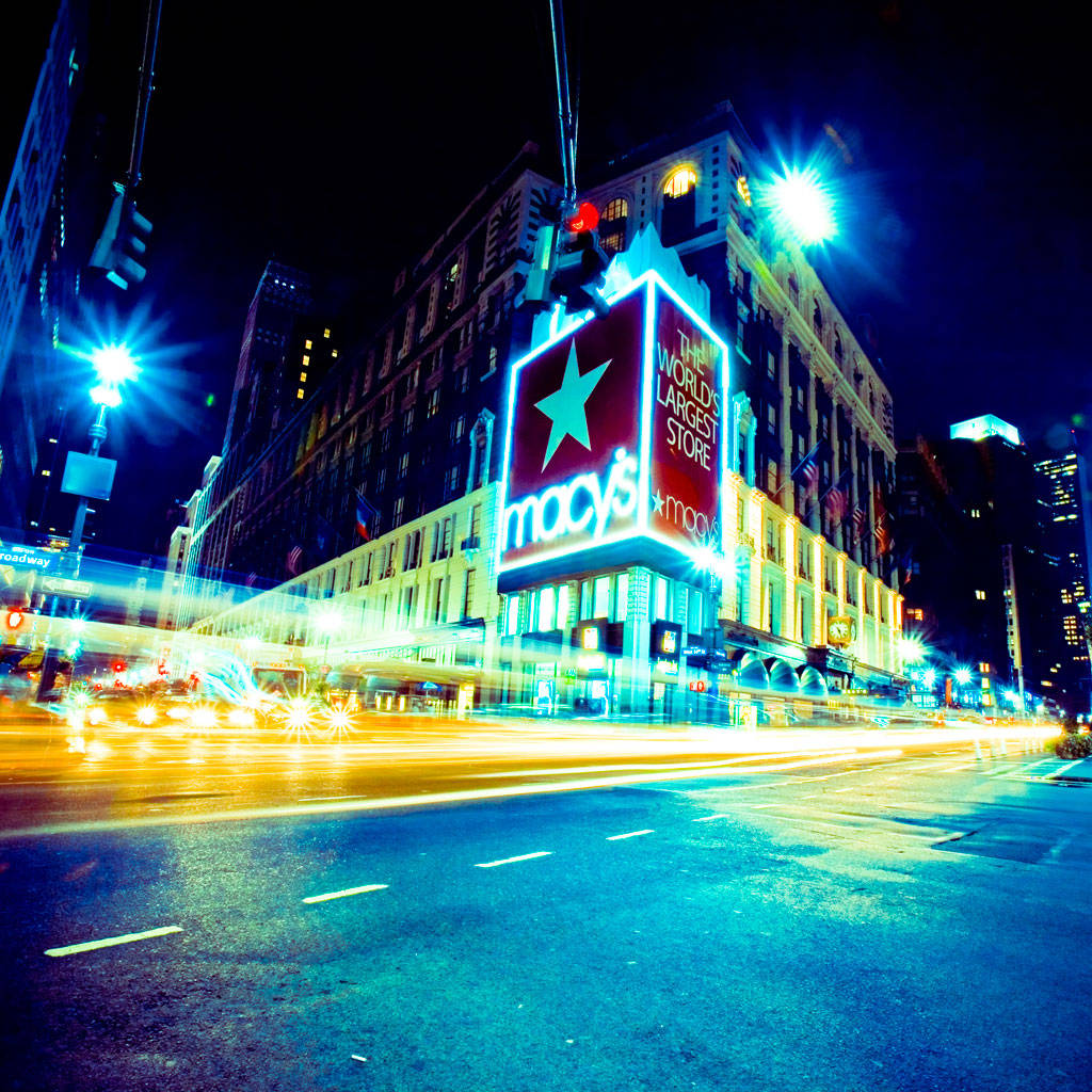 macys 桌布 壁紙 — 一張充滿活力的夜間照片，拍攝了梅西百貨公司，濕漉漉的城市街道上車燈流動。