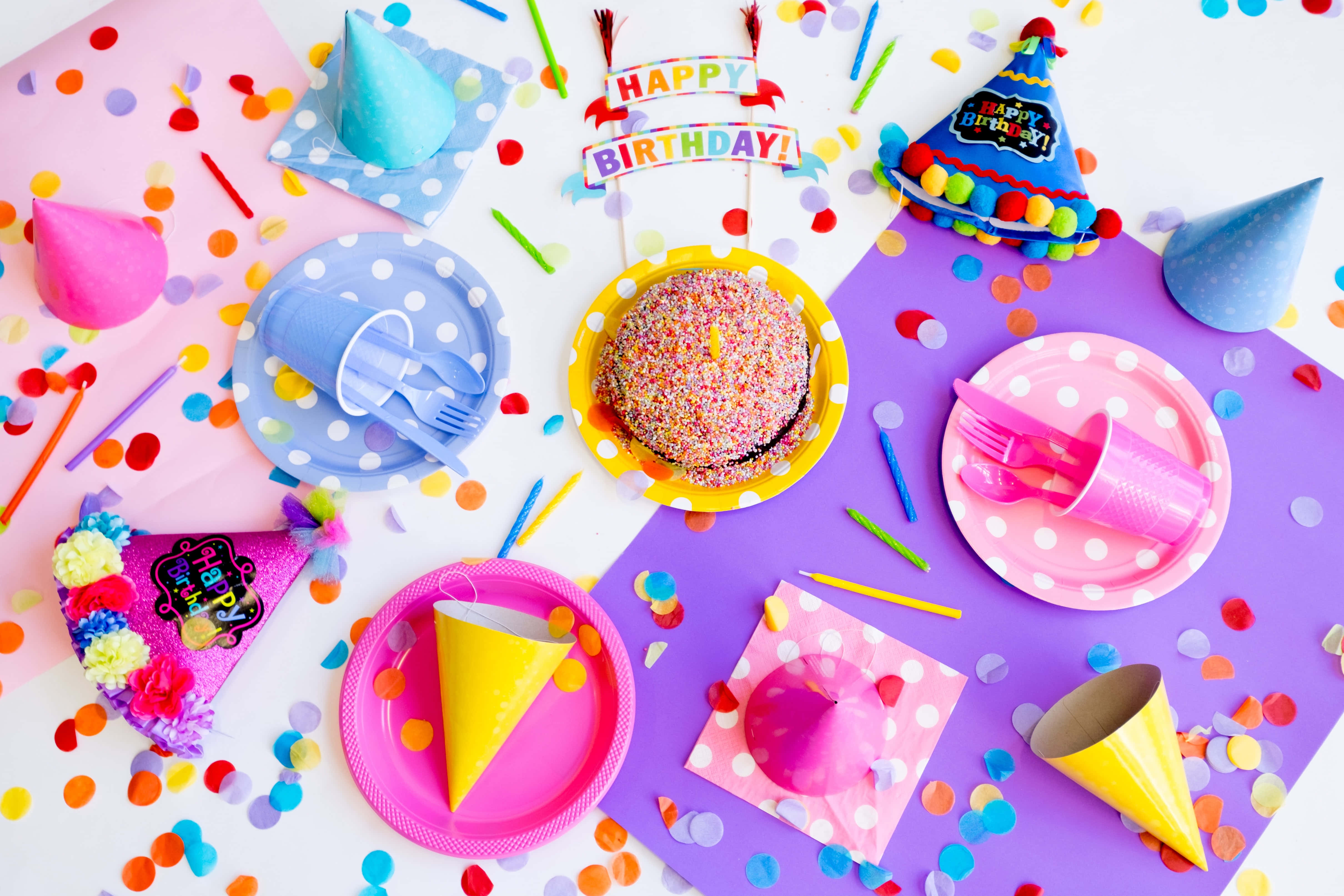 Cute Birthday 桌布 壁紙 — 一張充滿活力的生日派對俯拍，有色彩繽紛的盤子、杯子、帽子和一個撒滿糖粒的蛋糕，周圍環繞著五彩紙屑。