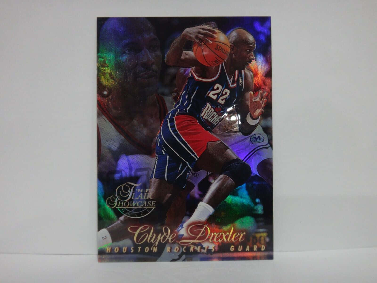 籃球 桌布 壁紙 — 一張充滿活力的籃球交易卡，展示 Clyde Drexler 在行動中，運球對抗防守者，帶有發光的霓虹背景效果。