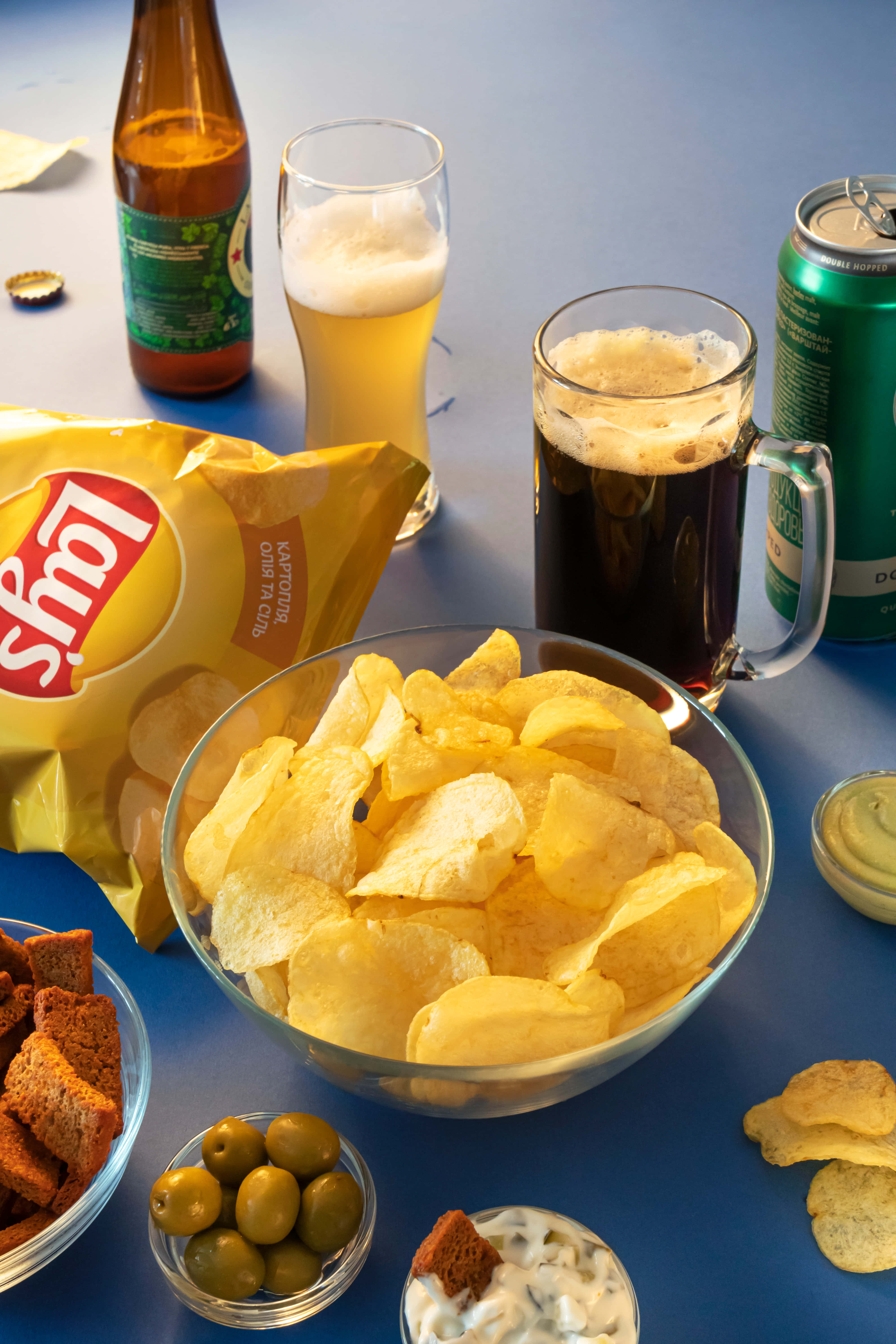 Snacks 桌布 壁紙 — 一張充滿活力的藍色桌子上放著一碗樂事洋芋片、啤酒、橄欖和蘸醬，營造出休閒零食場景。