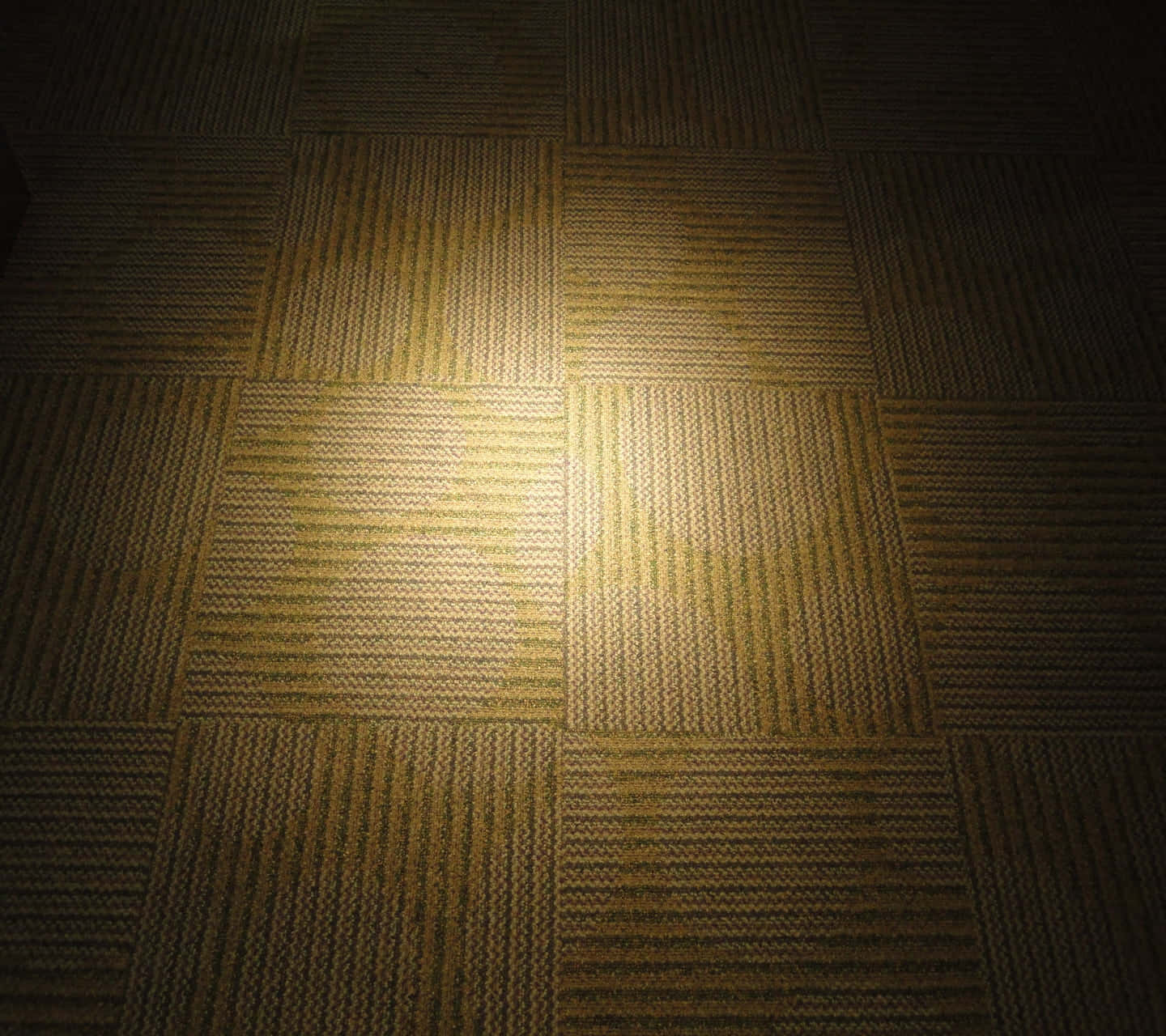 Carpet 桌布 壁紙 — 一張光線昏暗的編織地毯，方形瓷磚被單一暖色聚光燈照亮，形成強烈對比。