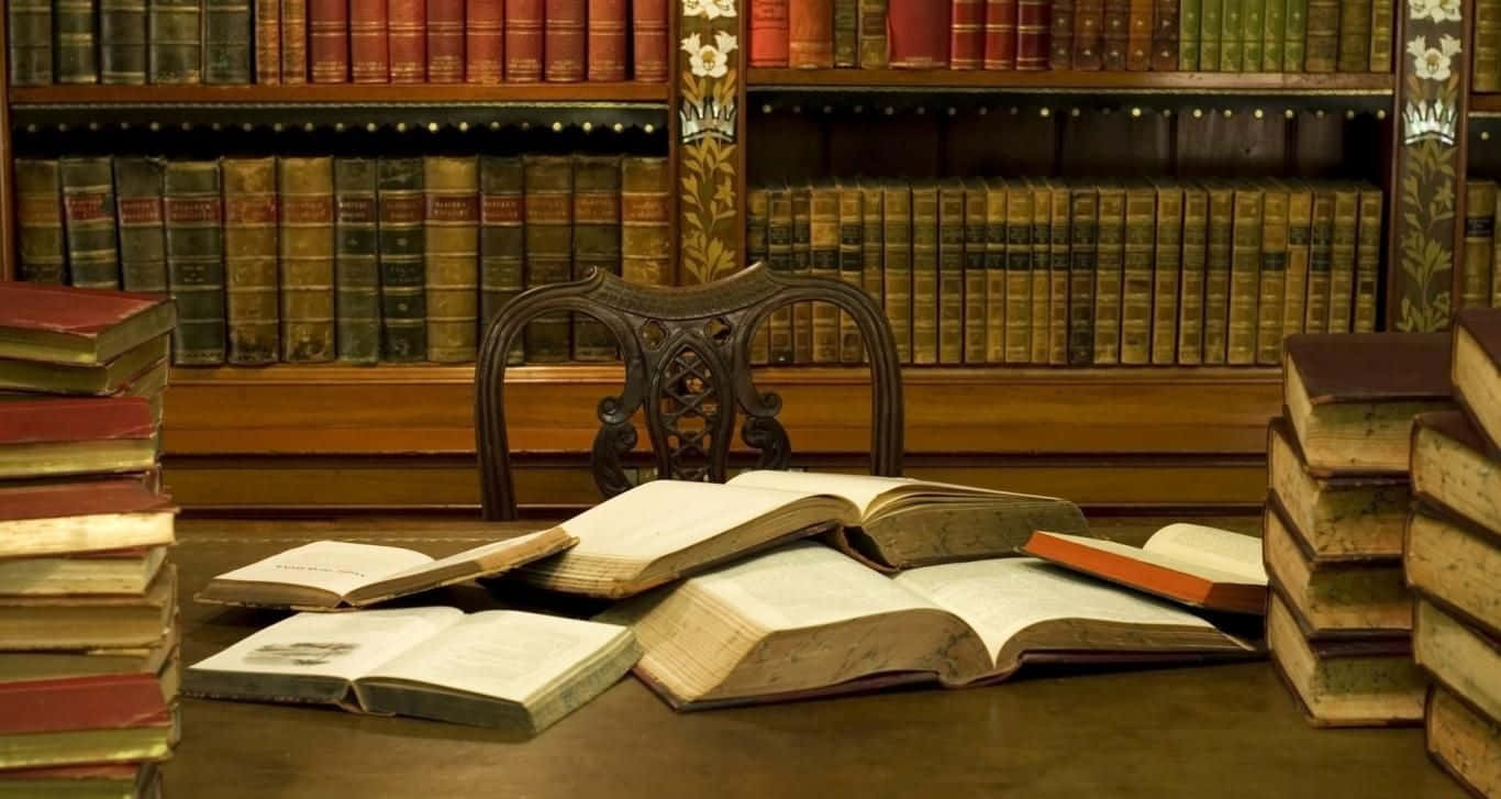 書本 桌布 壁紙 — 一張古董木椅坐落在昏暗的復古圖書館中，周圍散落著打開的書籍和高高的書堆。