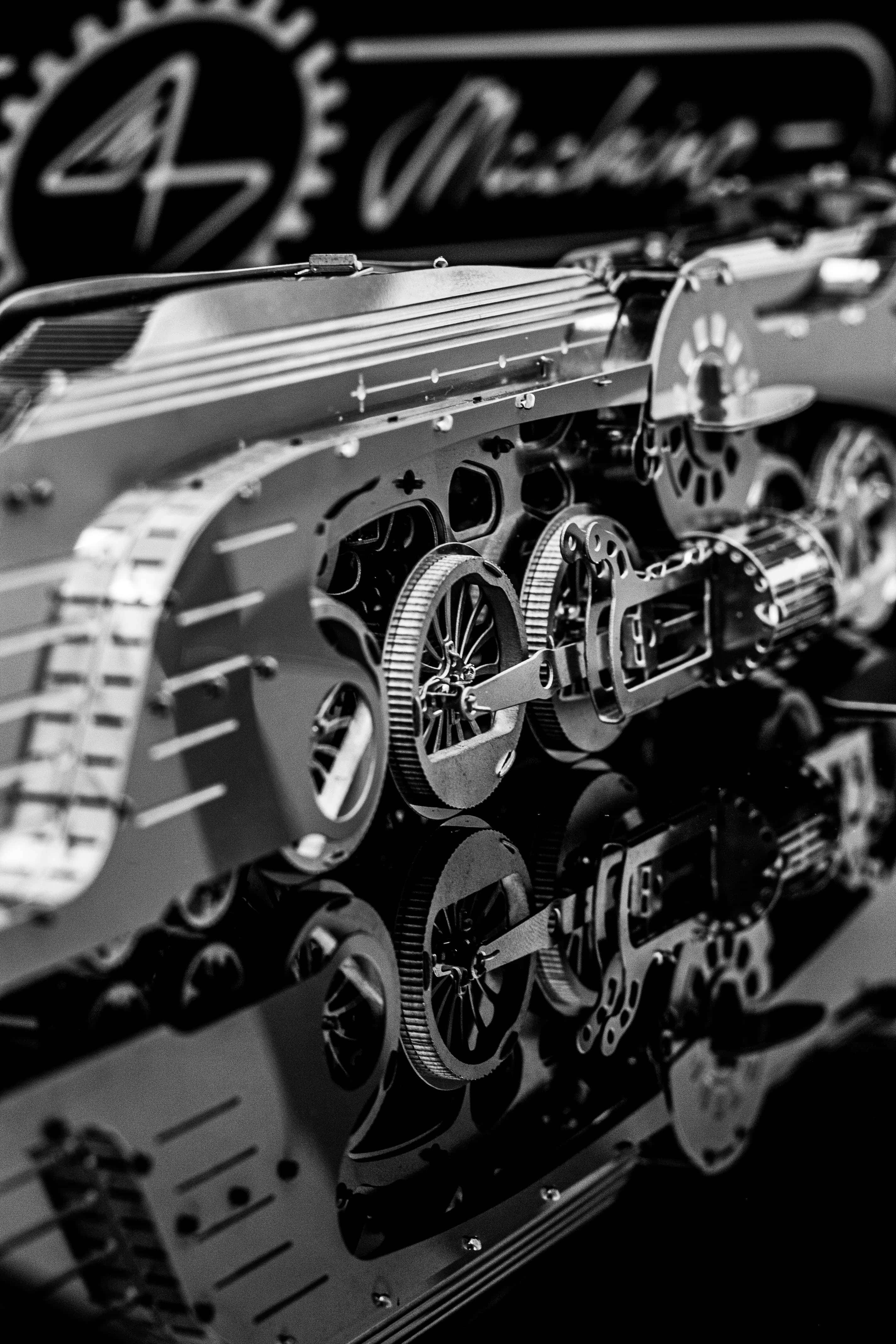 Mechanical Engineering 桌布 壁紙 — 一張單色特寫，展示複雜的機械齒輪和嵌齒在拋光表面上的倒影，背景有模糊的「Making」標誌。