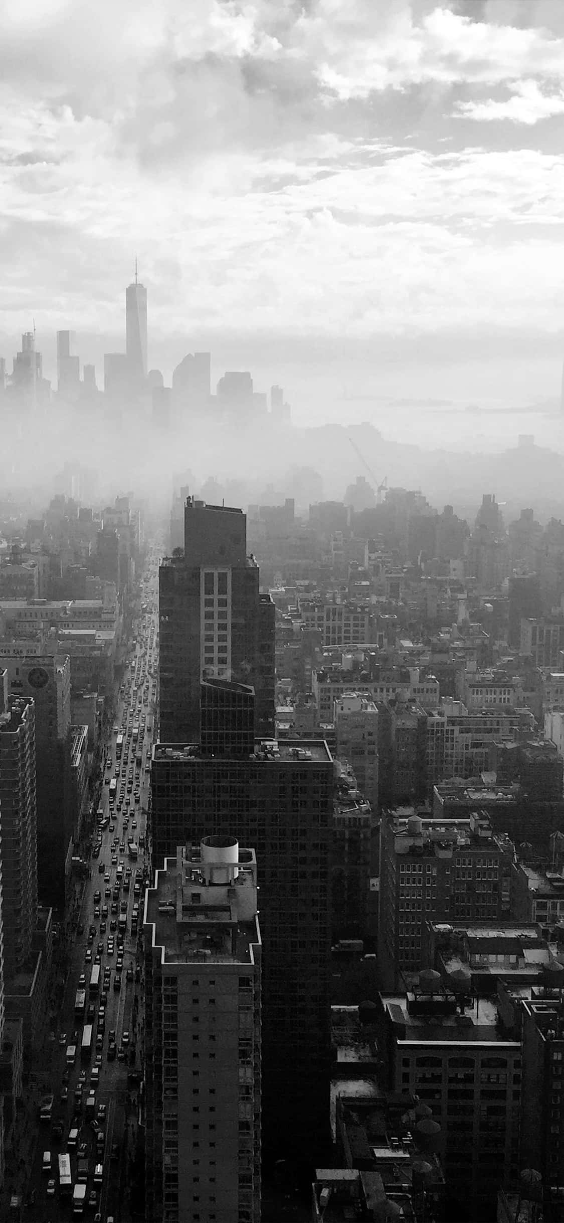 iPhone Xs New York 桌布 壁紙 — 一張單色鳥瞰圖，展現了被大氣薄霧籠罩的密集城市景觀，高聳的摩天大樓和下方繁忙的大道。