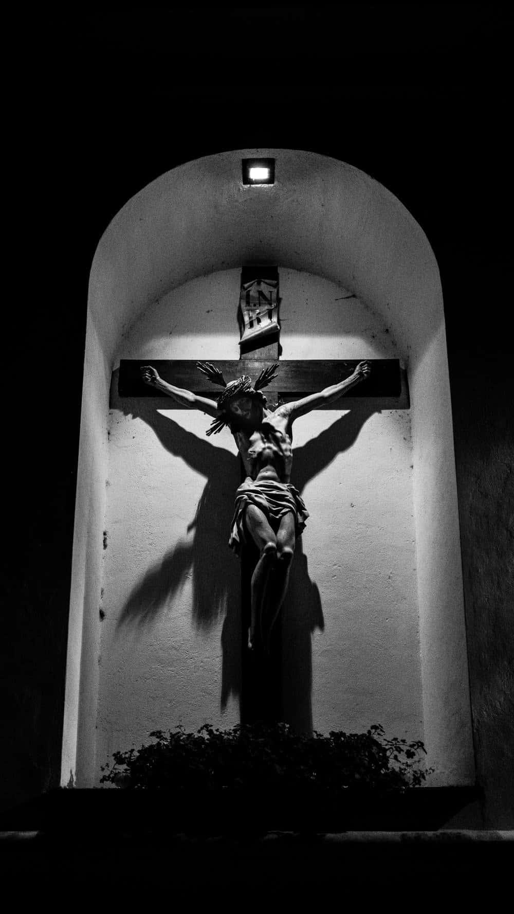 Jesus Crucifixion 桌布 壁紙 — 一張在石拱門內由單一燈光照亮的釘十字架雕像的清晰黑白照片。