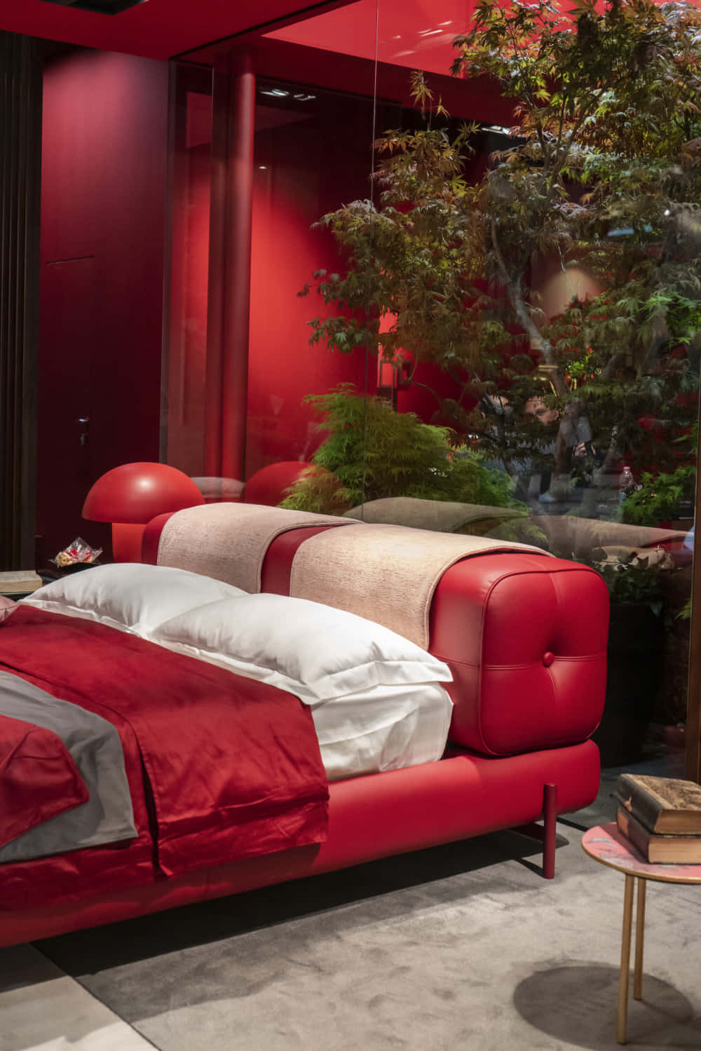 Red Room 桌布 壁紙 — 一張大膽的紅色皮革床搭配白色床單，位於現代臥室中，沐浴在深紅色的光線下，旁邊是一棵茂盛的室內樹。