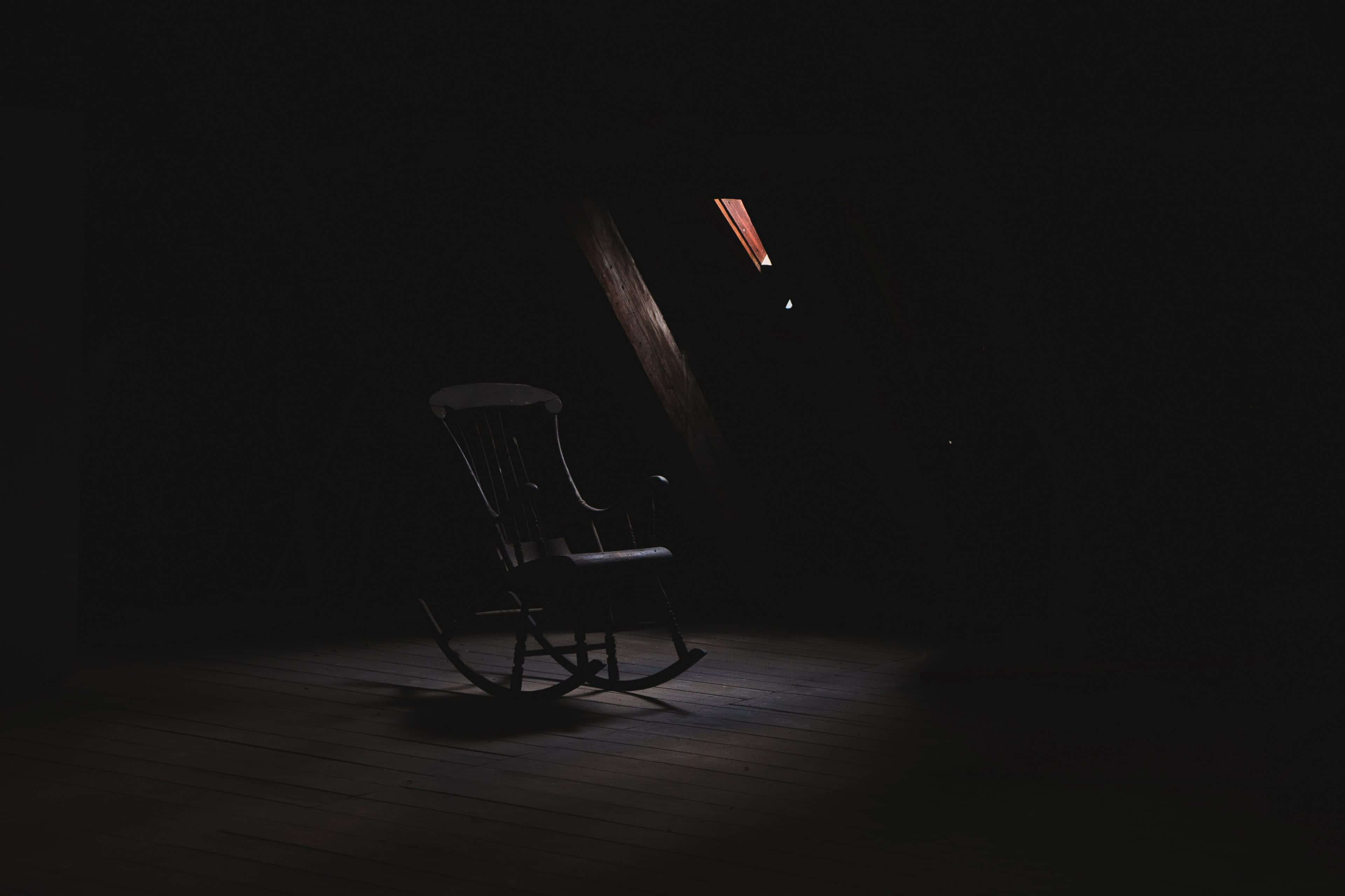 Dark Room 桌布 壁紙 — 一張孤獨的搖椅放在漆黑的閣樓裡，沐浴在高窗射下的一縷溫暖光線中。