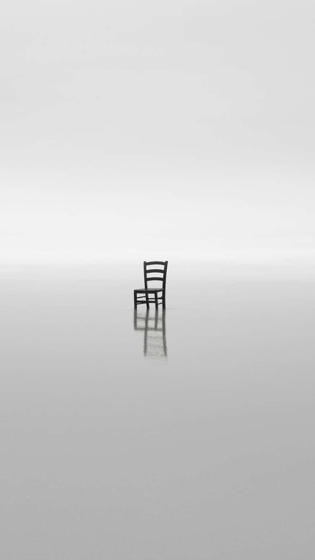 chair 桌布 壁紙 — 一張孤獨的木椅獨自站在廣闊的反射性灰色表面上，天空多雲。