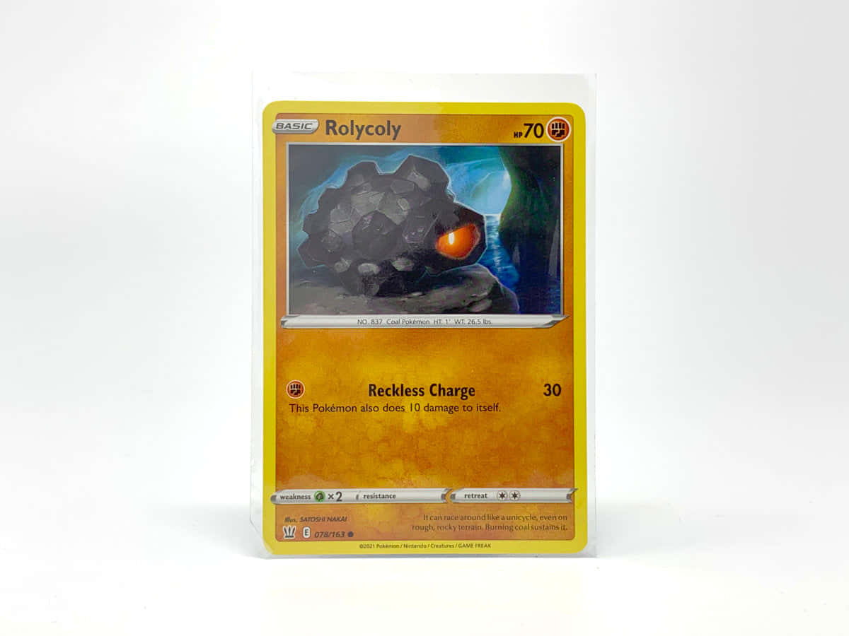 Cards 桌布 壁紙 — 一張密封的寶可夢集換式卡牌， featuring Rolycoly， 發光的橙色眼睛， 背景是黑暗的岩石。