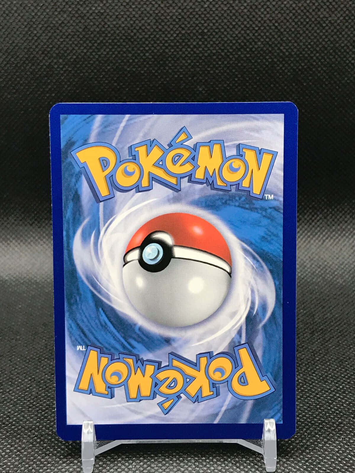 Pokemon Card 桌布 壁紙 — 一張寶可夢集換式卡牌，帶有旋轉的寶可夢球標誌，背景為藍色，直立展示在支架上。