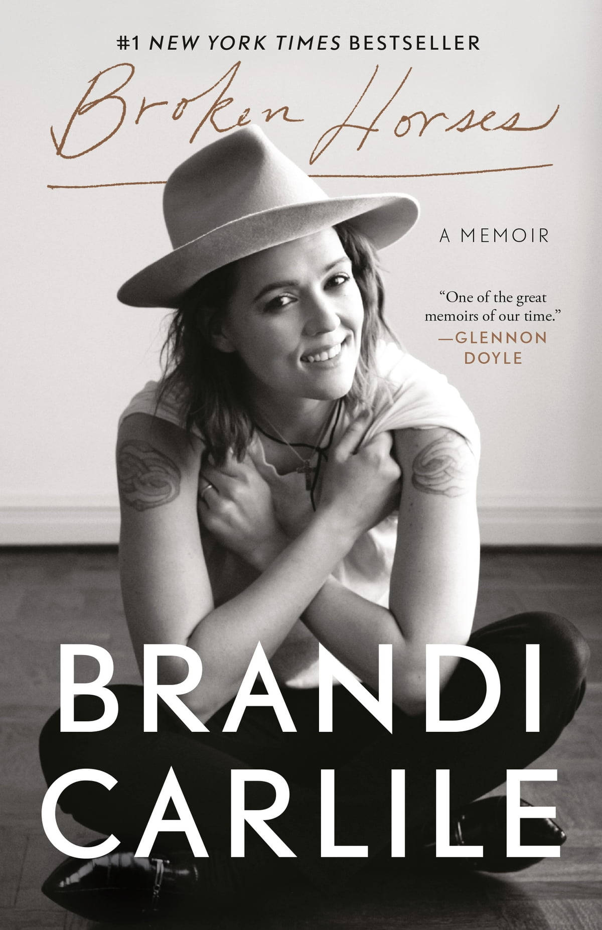Brandi 桌布 壁紙 — 一張布蘭迪·卡萊爾（Brandi Carlile）微笑盤腿而坐、戴著寬邊帽、手臂上可見刺青的黑白肖像。