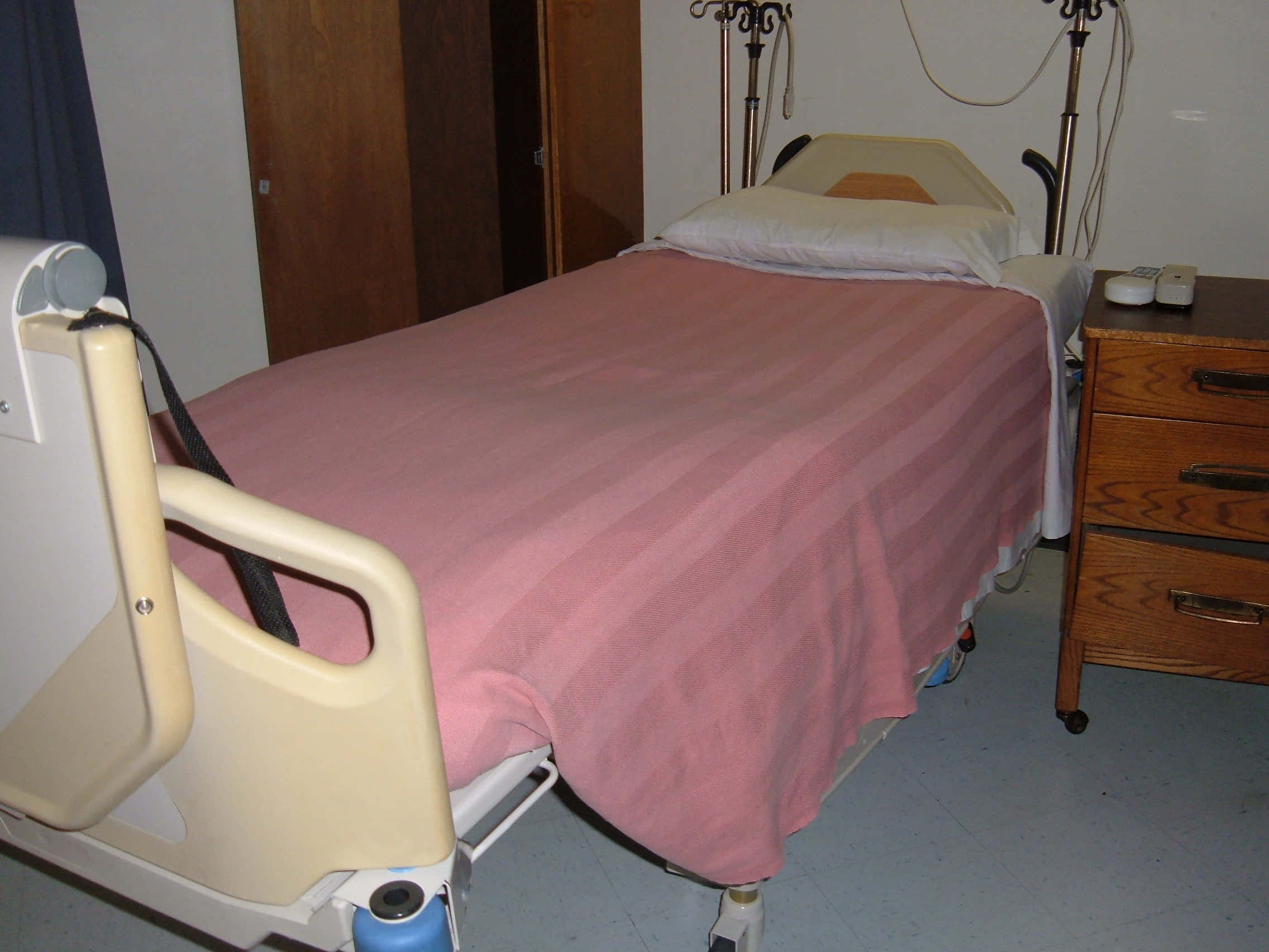 Hospital 桌布 壁紙 — 一張帶有粉紅色條紋毯子的醫院病床放在臨床房間內，旁邊有木製床頭櫃和醫療設備。