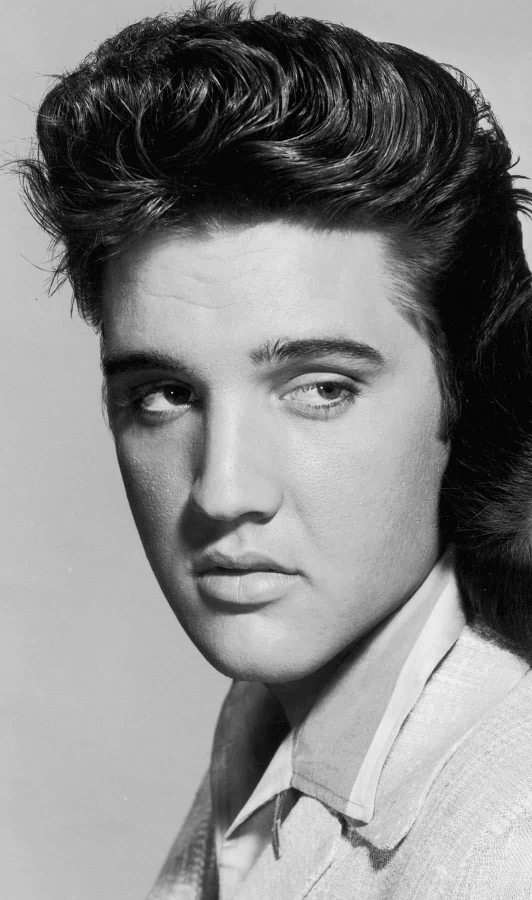 Black And White Celebrity 桌布 壁紙 — 一張年輕貓王艾維斯·普里斯萊的黑白肖像，帶有標誌性的蓬巴杜髮型和強烈眼神。