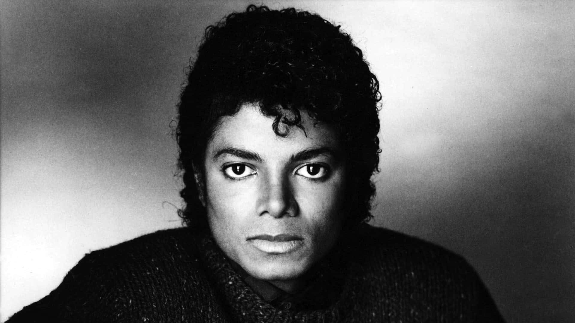 Young Michael Jackson 桌布 壁紙 — 一張引人注目的麥可傑克森黑白肖像，他捲曲的頭髮和質感毛衣在柔和漸變背景前凝視著。