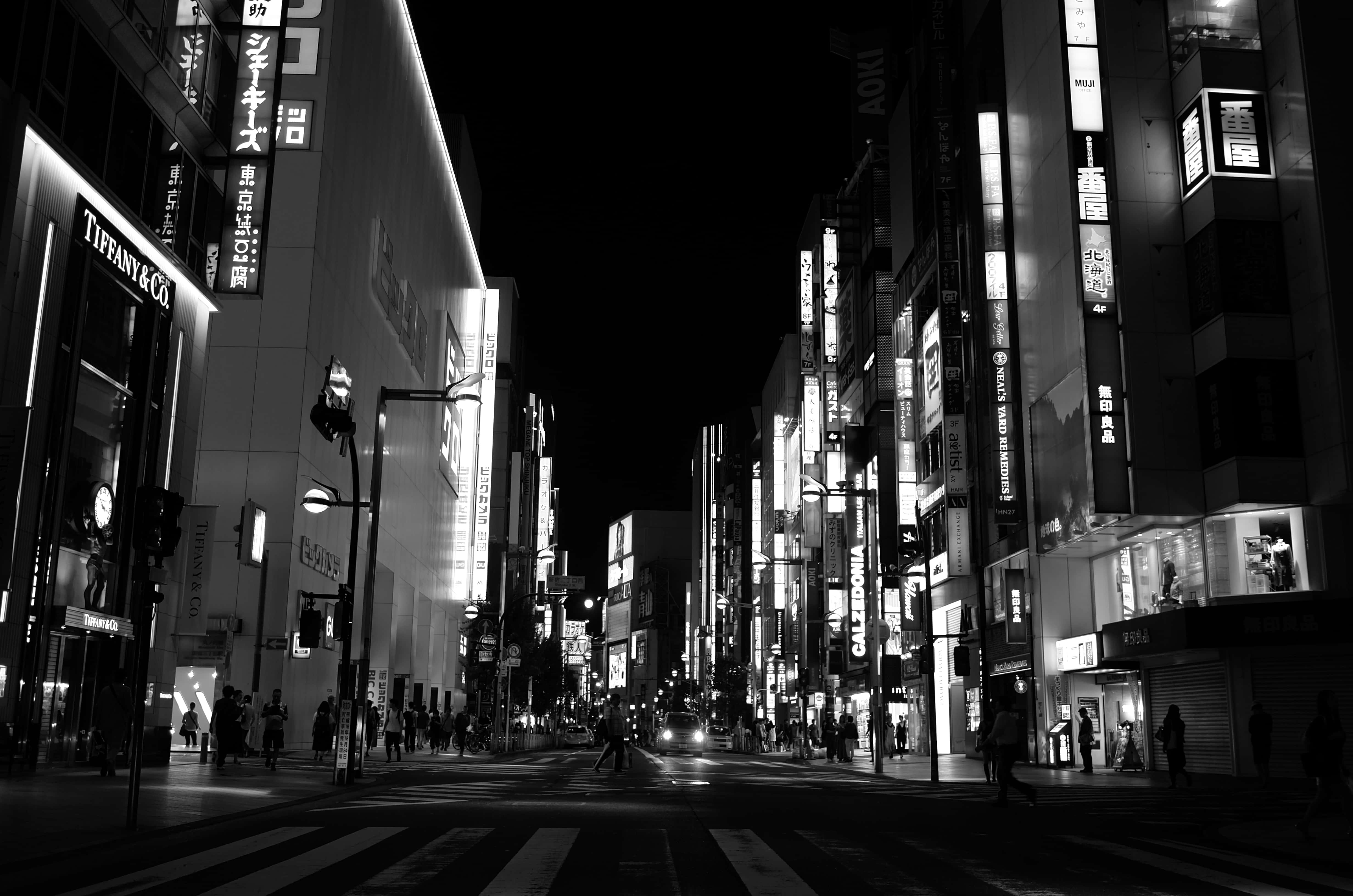 日本黑白 桌布 壁紙 — 一張引人注目的黑白夜景照片，拍攝了東京一條繁華的街道，兩旁是高聳的建築物和發光的霓虹燈招牌。