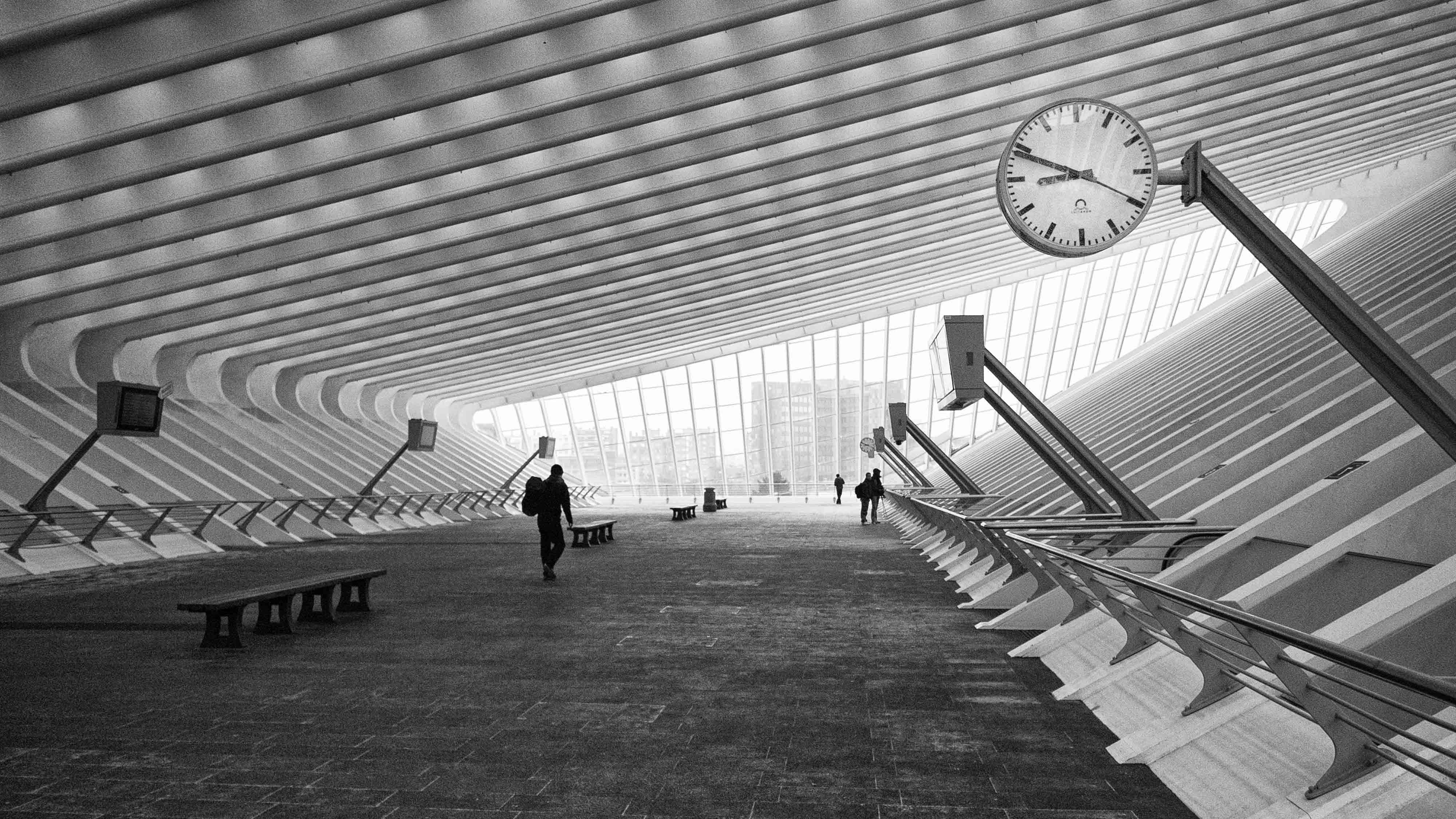 Black And White Architecture 桌布 壁紙 — 一張引人注目的黑白照片，展示了一個現代建築空間，有一個大時鐘，人們在帶肋條的天花板下行走。