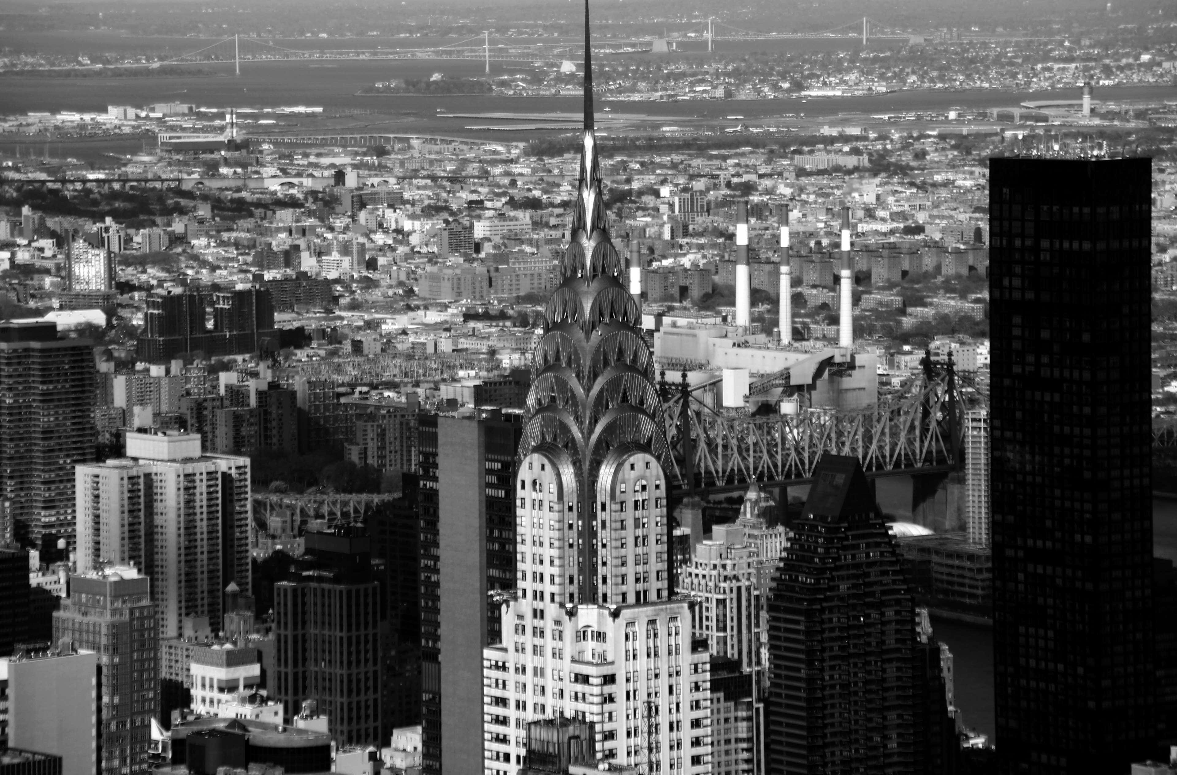 Black And White Cityscape 桌布 壁紙 — 一張引人注目的黑白空中照片，克萊斯勒大廈聳立在密集的紐約市天際線上，背景有橋樑和遠處的水域。