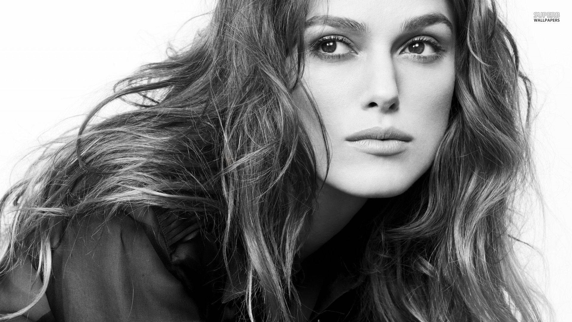 Keira Knightley 桌布 壁紙 — 一張引人注目的黑白肖像，一位頭髮被風吹拂的女人專注地凝視著相機。