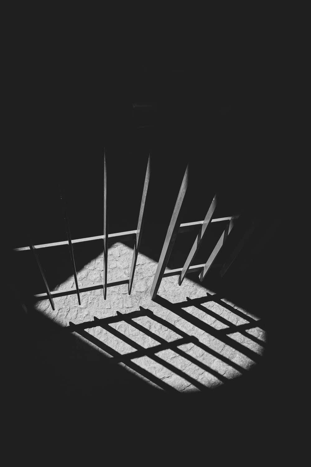 Prison Cell 桌布 壁紙 — 一張強烈對比的黑白照片，顯示欄杆在深暗處投射在紋理地板上的銳利幾何陰影。