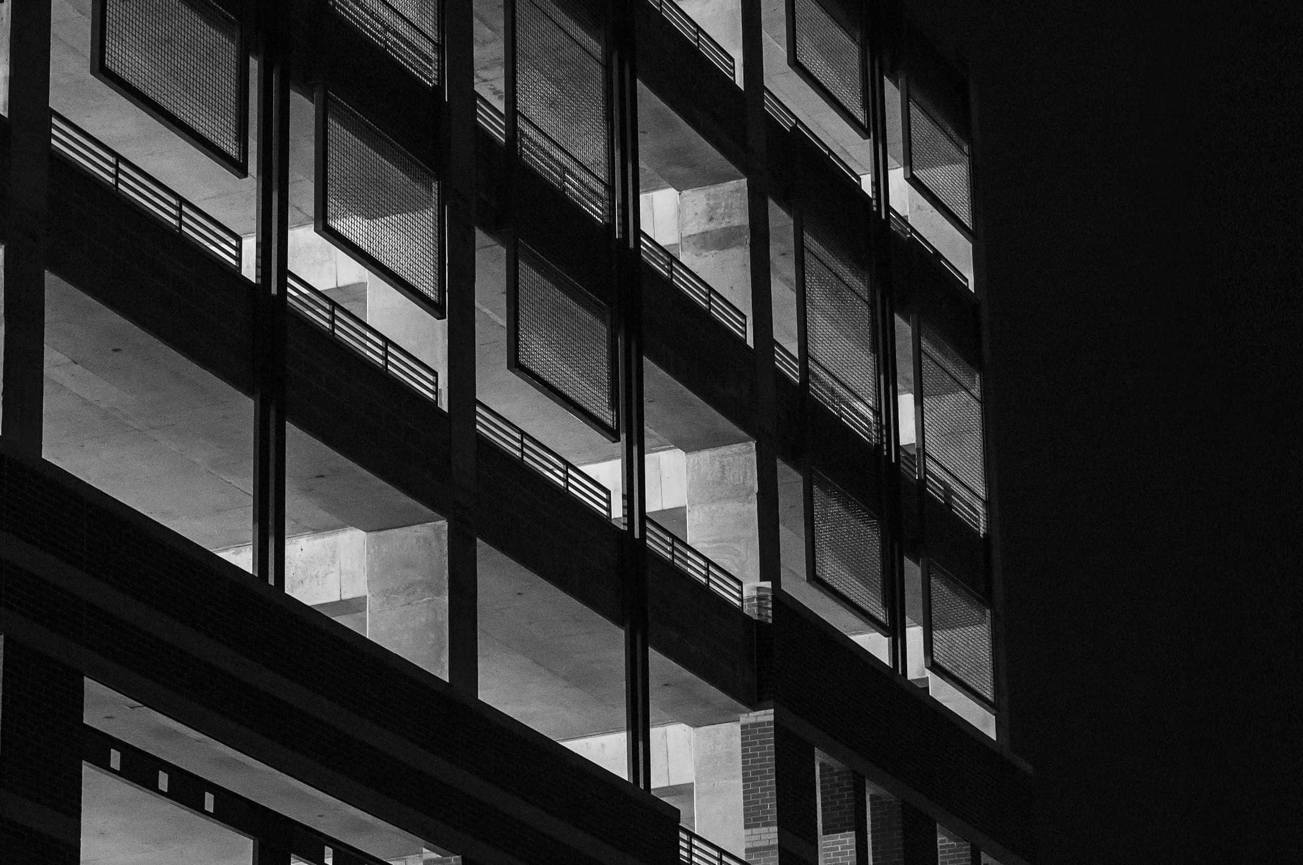 Black And White Architecture 桌布 壁紙 — 一張強烈黑白對比的建築照片，拍攝夜晚的多層建築，帶有強烈的幾何陰影和明亮的窗戶。