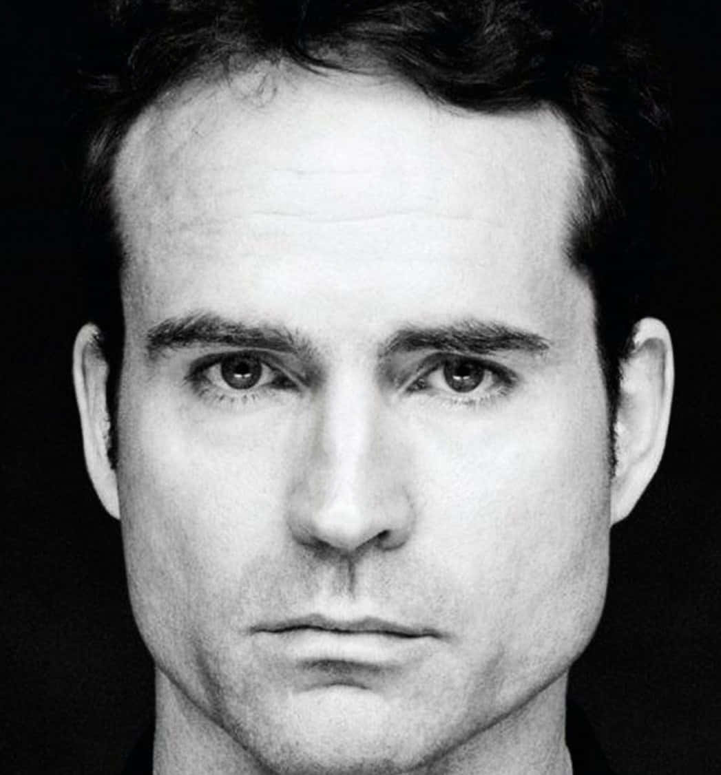 Jason Patric 桌布 壁紙 — 一張強烈黑白特寫肖像，捕捉一位眼神銳利、表情嚴肅的男子，背景為深色。