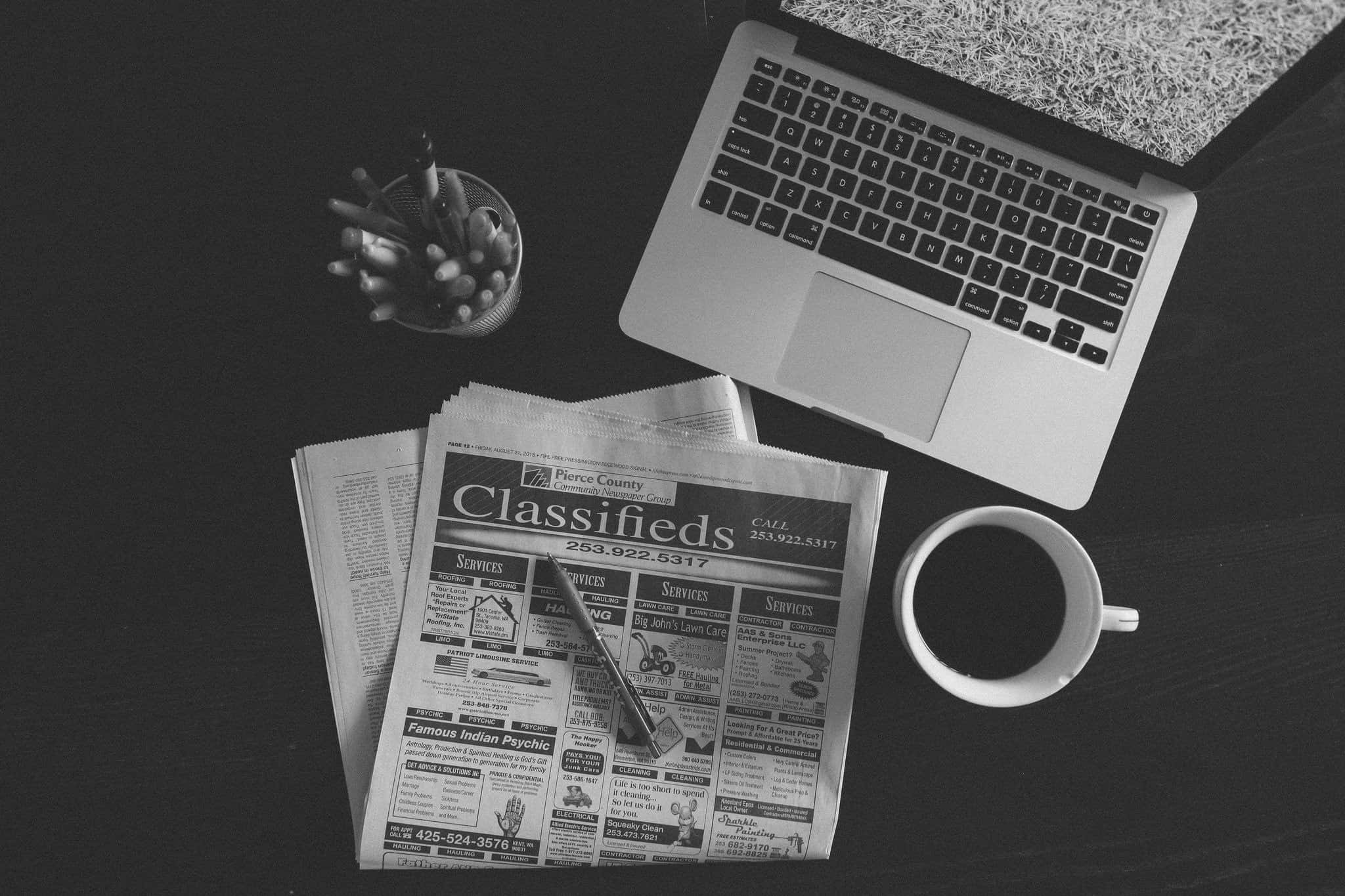 Black And White Newspaper 桌布 壁紙 — 一張從上方拍攝的單色照片，顯示深色書桌上的筆記型電腦、報紙分類廣告和咖啡杯。