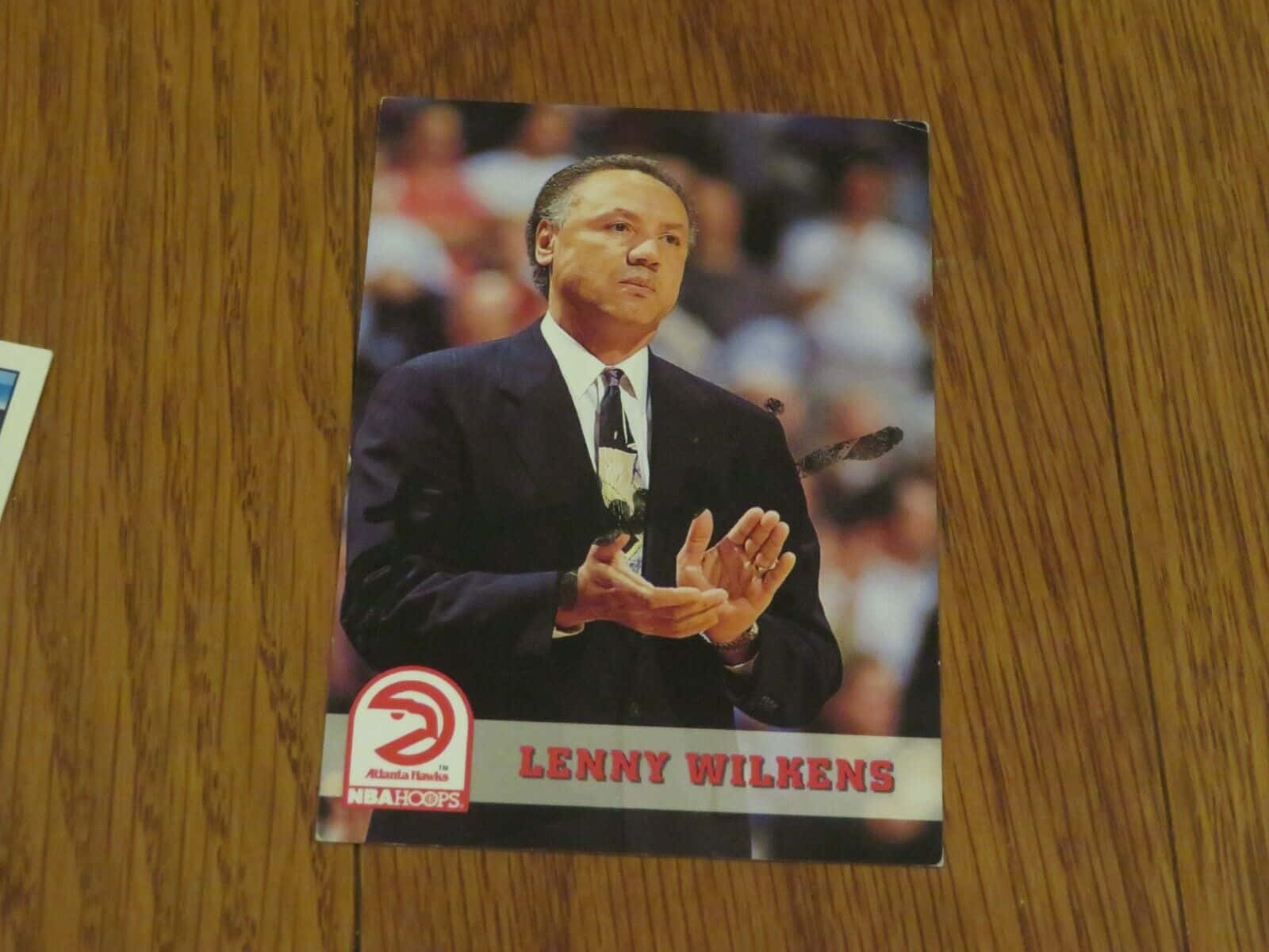 card 桌布 壁紙 — 一張復古NBA Hoops交易卡，展示身穿西裝的教練Lenny Wilkens在籃球場上做手勢，放在木桌上。