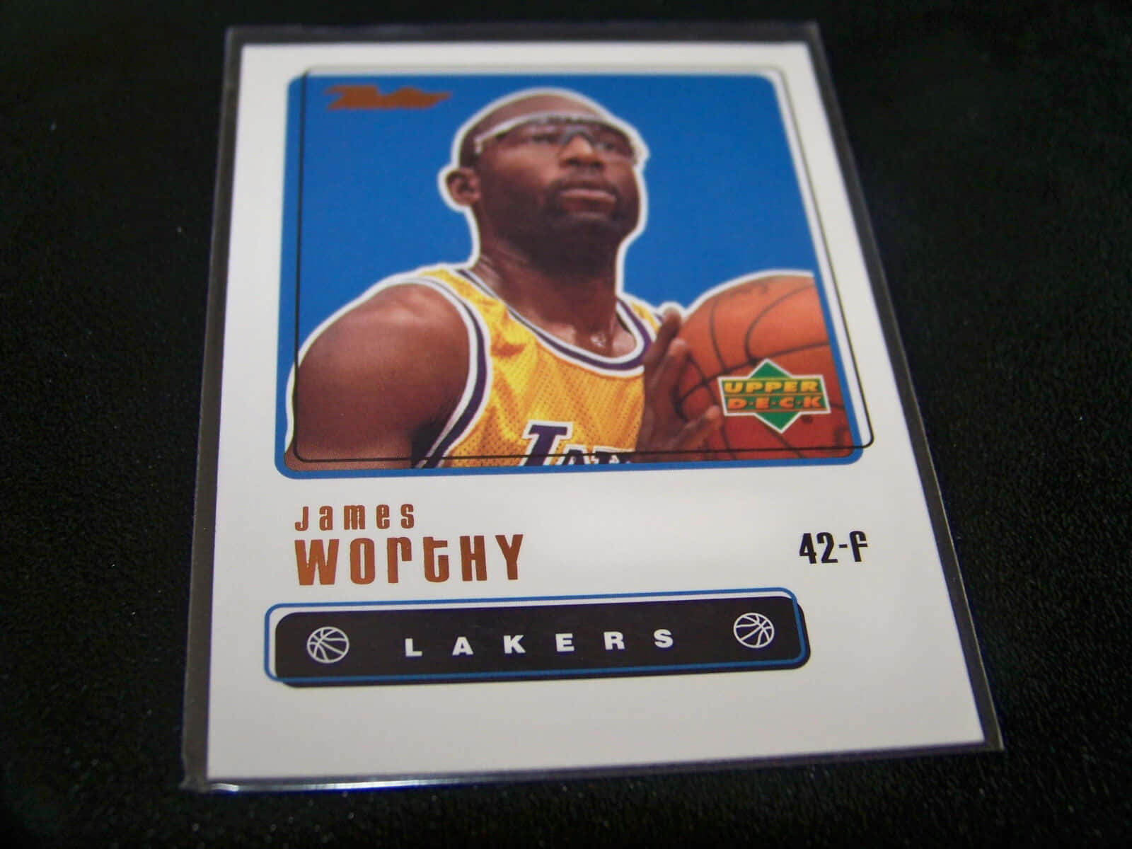 籃球 桌布 壁紙 — 一張復古Upper Deck籃球卡，展示身穿黃色湖人隊球衣的James Worthy，手持籃球，背景為藍色。