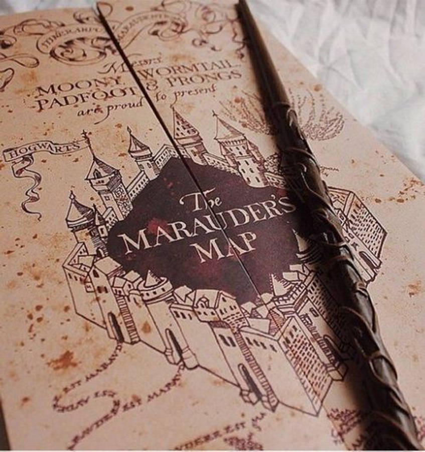 Marauders Map 桌布 壁紙 — 一張復古劫盜地圖，帶有複雜的霍格華茲插圖，放在陳舊羊皮紙上，上面有一根深色木魔杖。