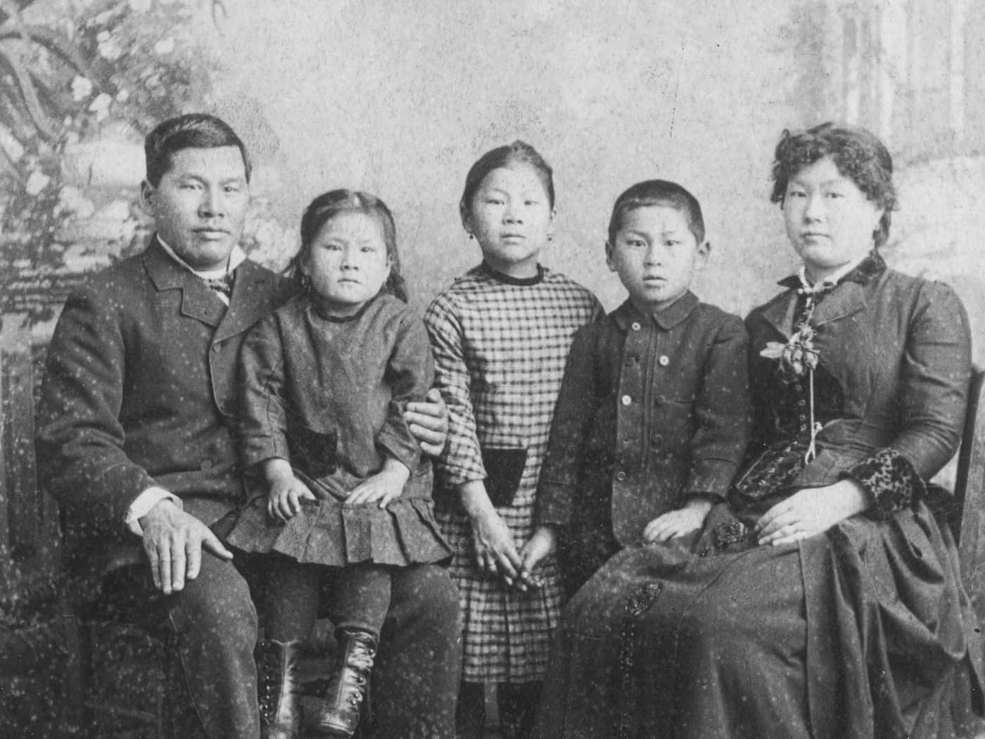 Family 桌布 壁紙 — 一張復古棕褐色調的家庭肖像，五個人正式坐在繪有花卉元素的背景前。