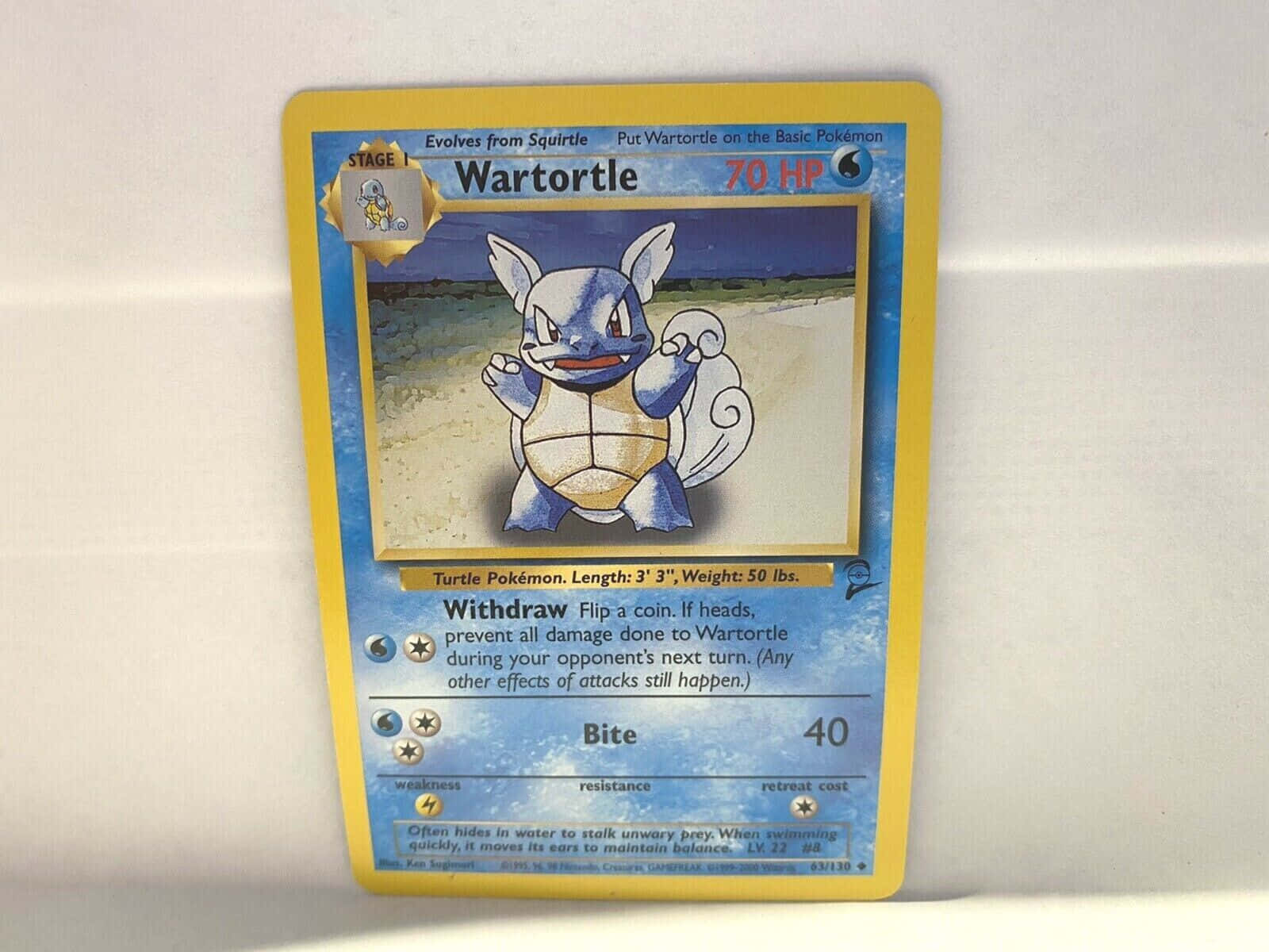 wartortle 桌布 壁紙 — 一張復古的Wartortle寶可夢交易卡，帶有藍色和黃色設計，放在純白色的表面上。