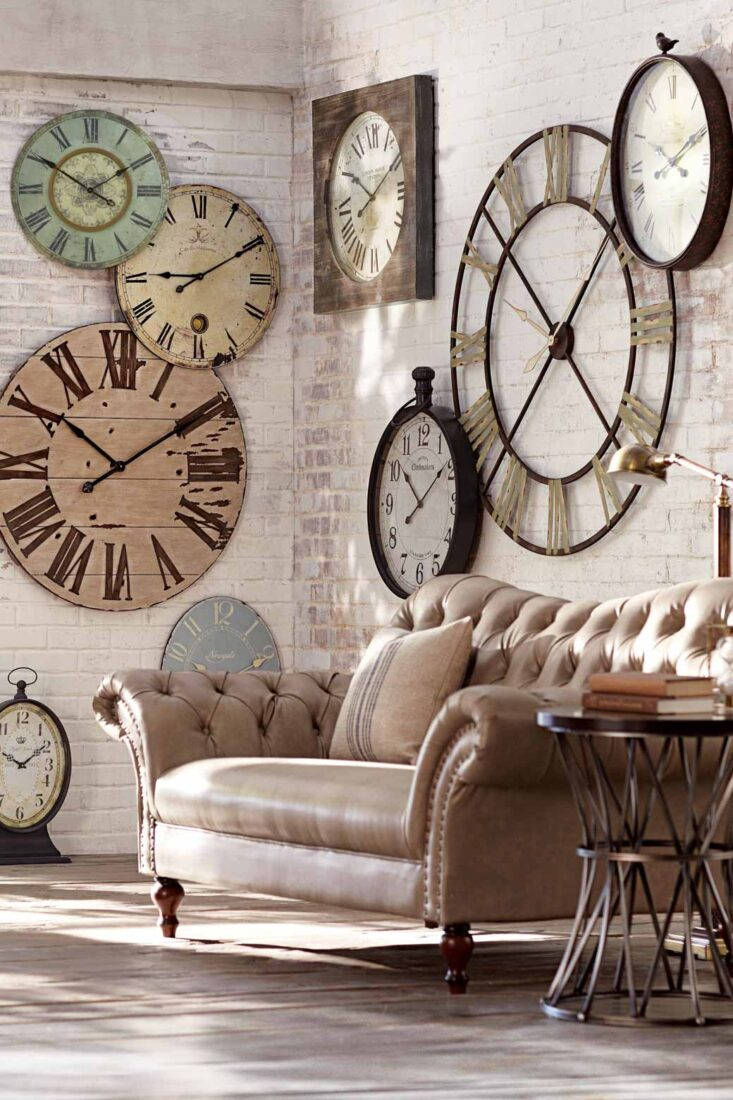 Clocks 桌布 壁紙 — 一張復古簇絨皮革沙發放在一面裝飾著各種質樸華麗時鐘的白色磚牆下。