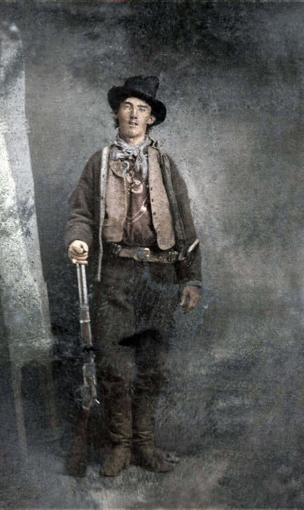 Old Western 桌布 壁紙 — 一張復古肖像，年輕牛仔戴著深色帽子和背心，在煙霧繚繞的攝影棚背景中手持步槍。