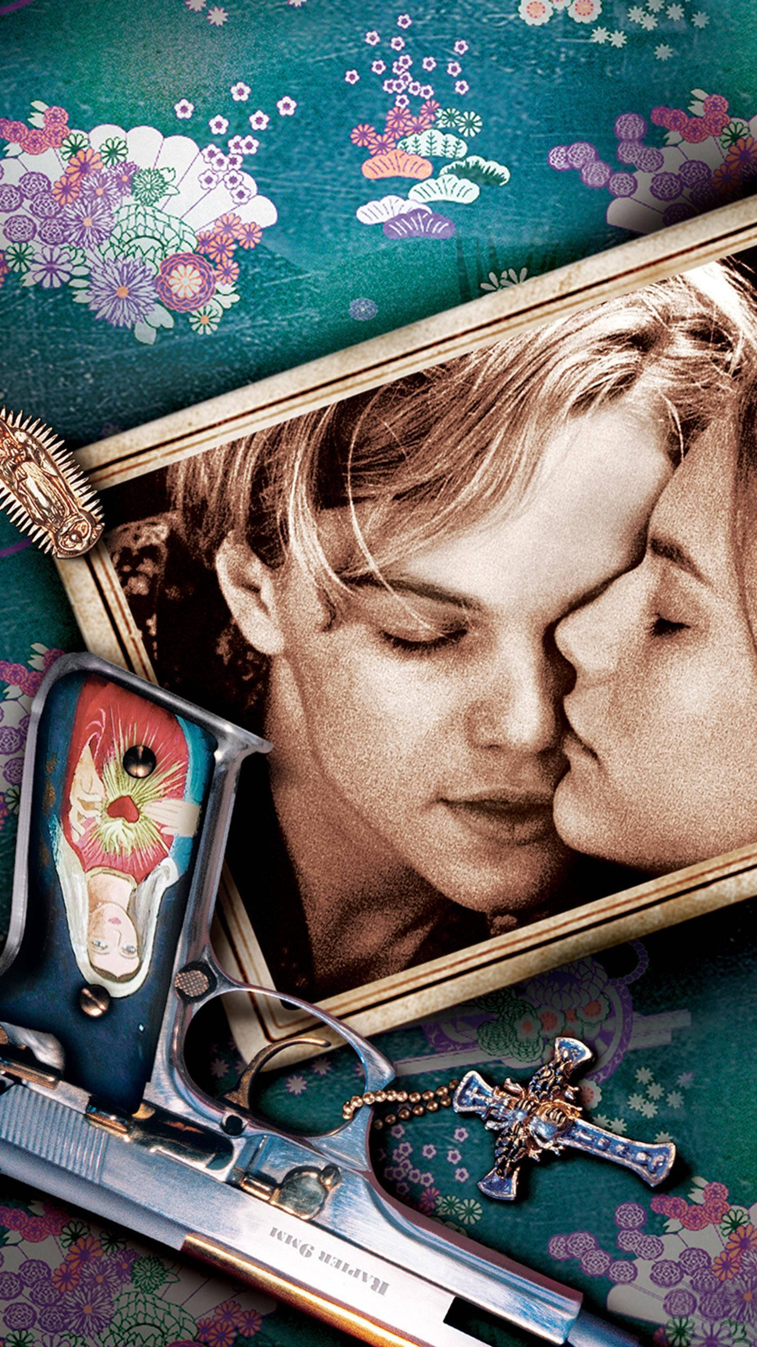 romeo and juliet 桌布 壁紙 — 一張復古色調的兩人接吻照片放在花卉圖案表面上，旁邊有一把裝飾過的手槍和一個十字架。