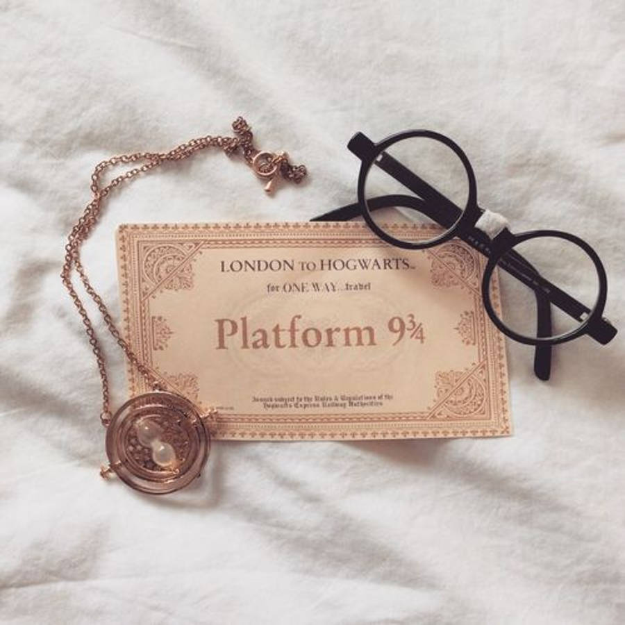 hp aesthetic 桌布 壁紙 — 一張復古風格的9¾月台車票放在白色布料上，旁邊有一個玫瑰金時光器和圓形黑色眼鏡。