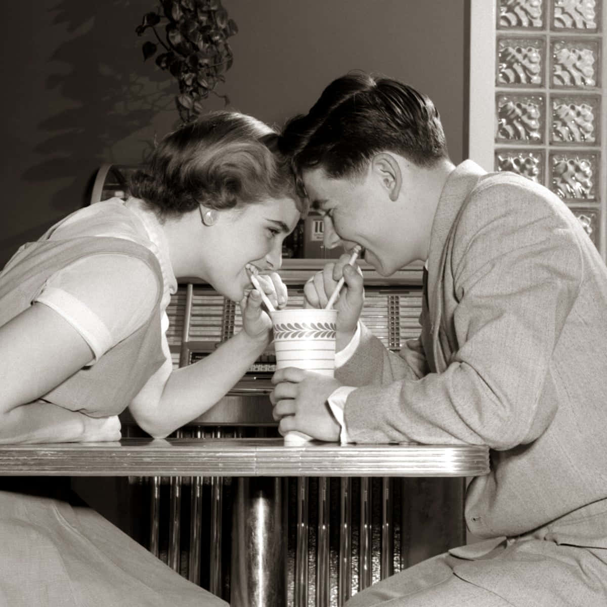 1950s 桌布 壁紙 — 一張復古黑白照片，一對年輕情侶在餐廳卡座用吸管分享飲料。