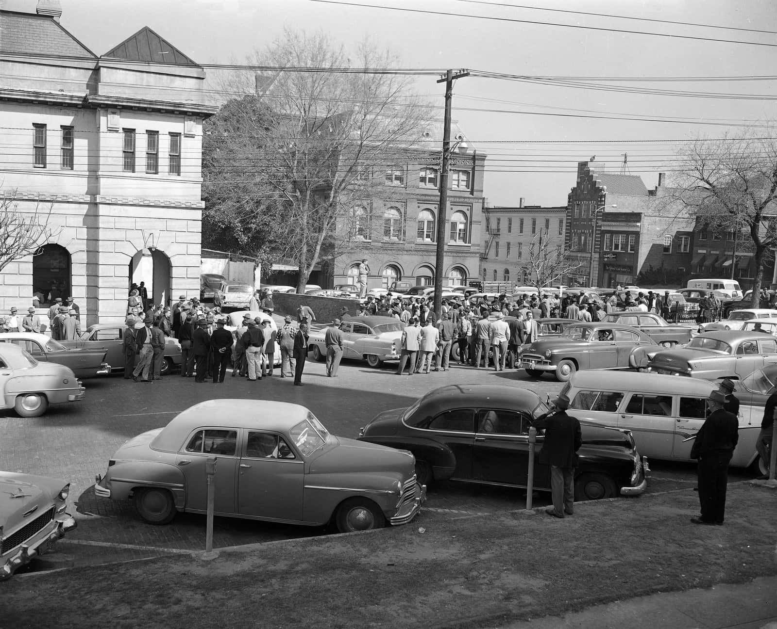 Black And White Vintage Car 桌布 壁紙 — 一張復古黑白照片，展現1950年代繁忙街道，充滿經典汽車和人群，靠近歷史建築。