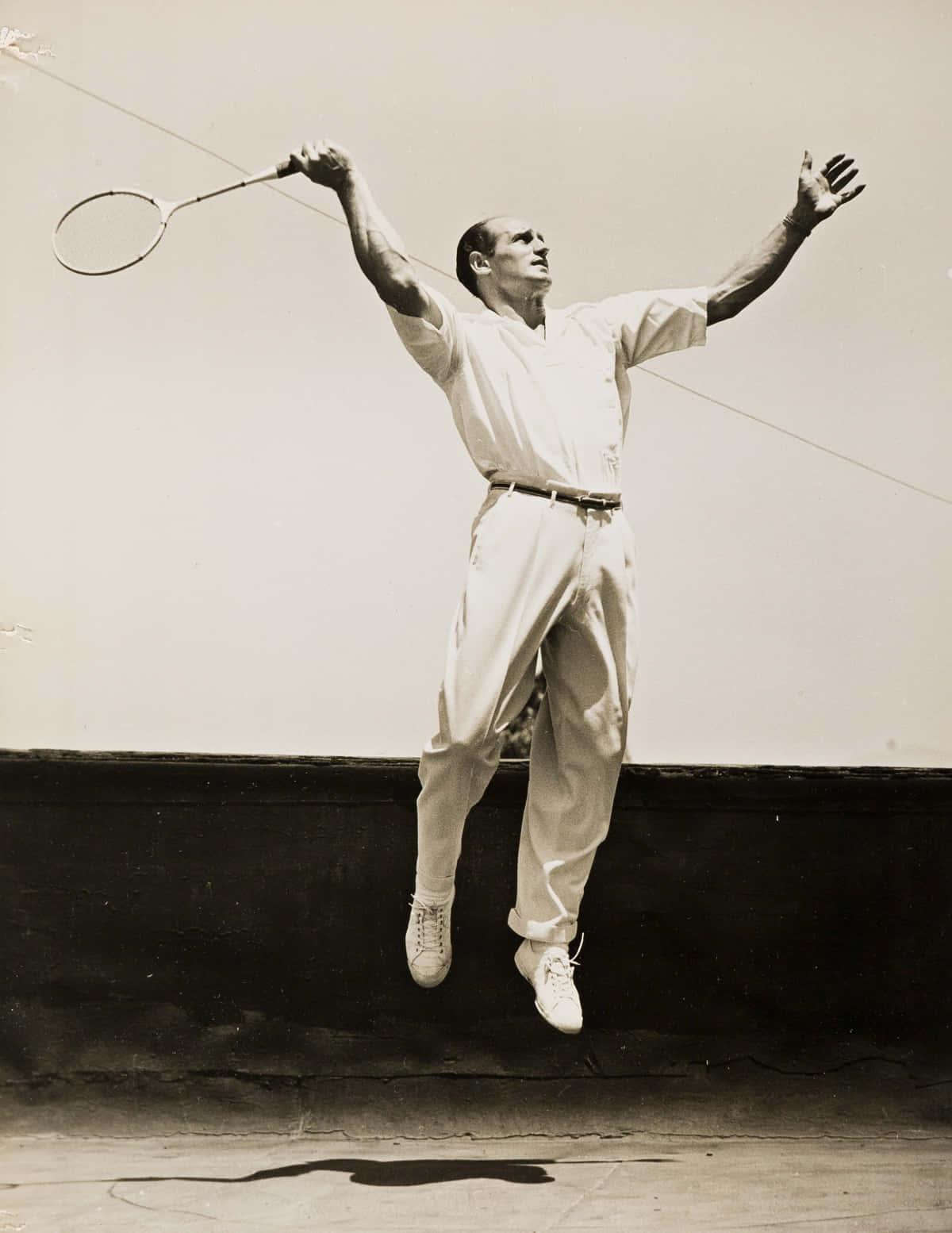 Tennis 桌布 壁紙 — 一張復古黑白照片中，一名男子在空中高高躍起，向著素牆揮動羽毛球拍。