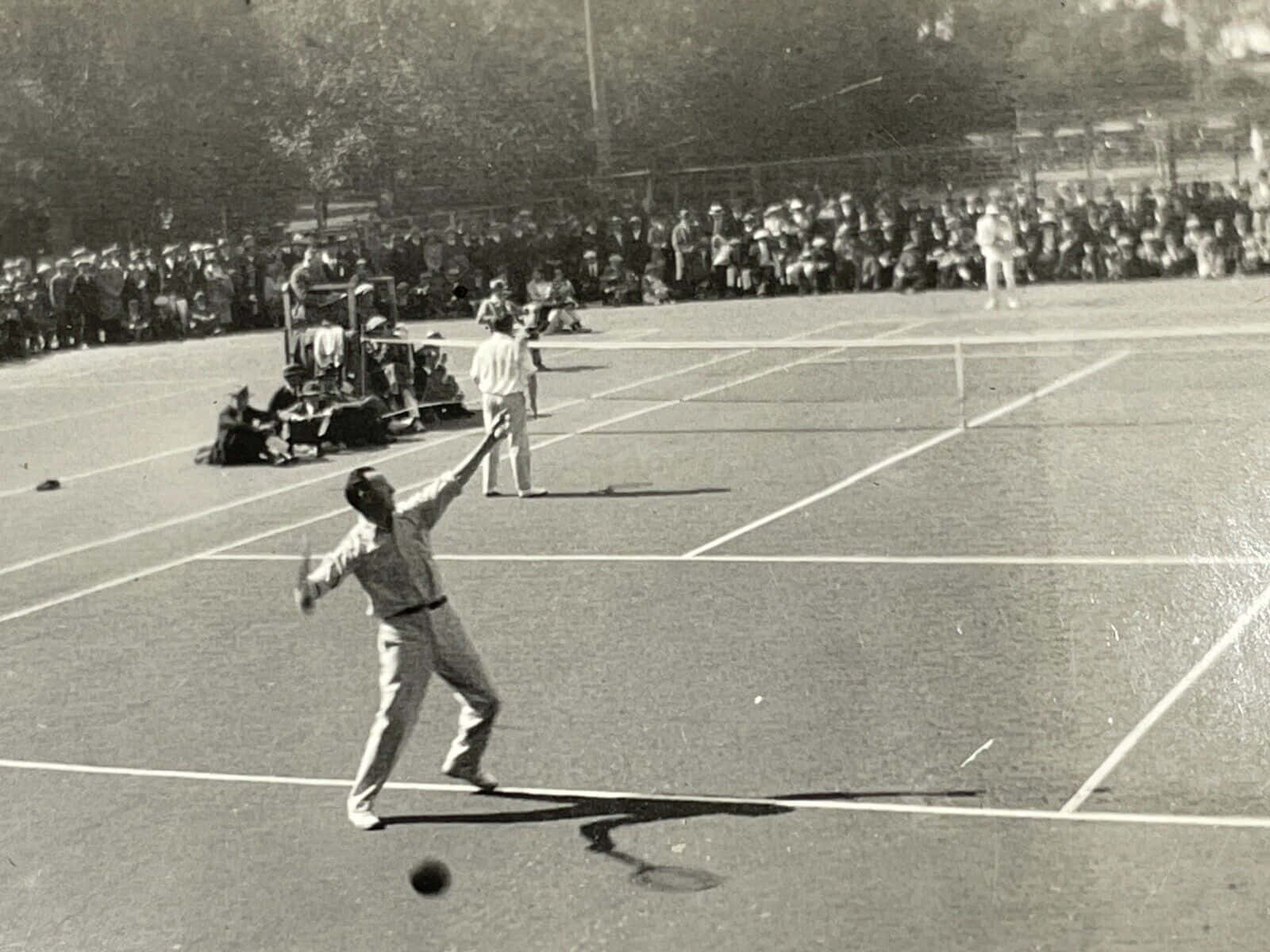 Tennis 桌布 壁紙 — 一張復古黑白照片捕捉到一位網球運動員在陽光明媚的戶外球場上發球，觀眾在觀看。