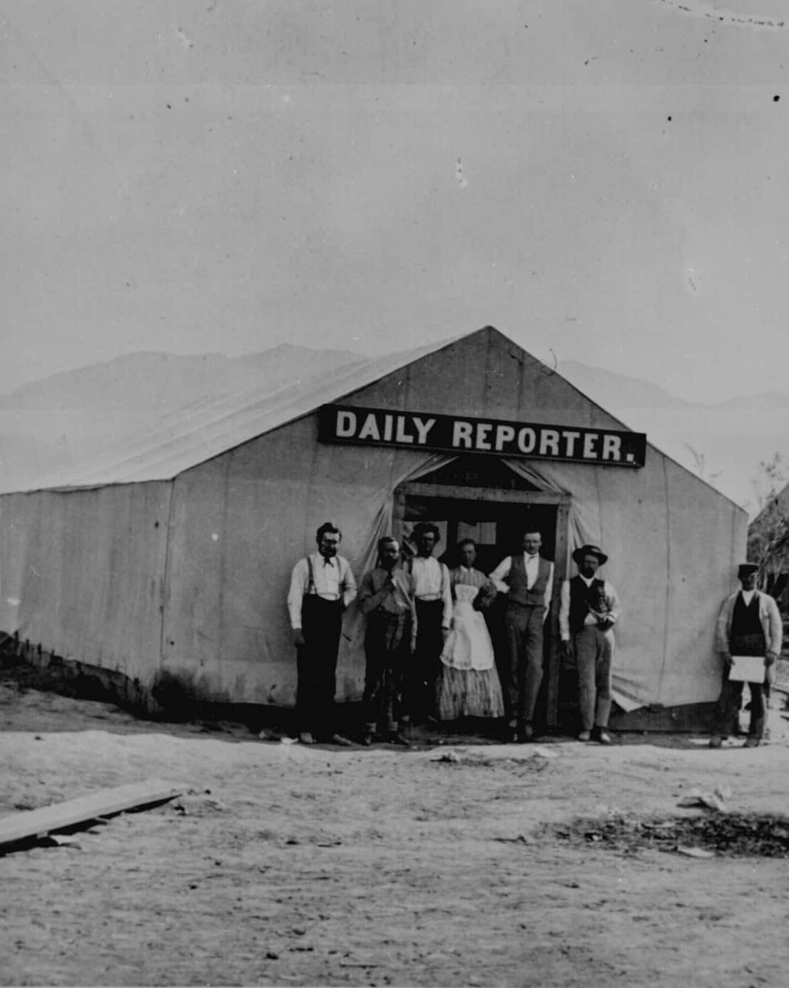 Old Western 桌布 壁紙 — 一張復古黑白照片顯示七個人在標有「DAILY REPORTER」的帳篷前擺姿勢，背景有山脈。