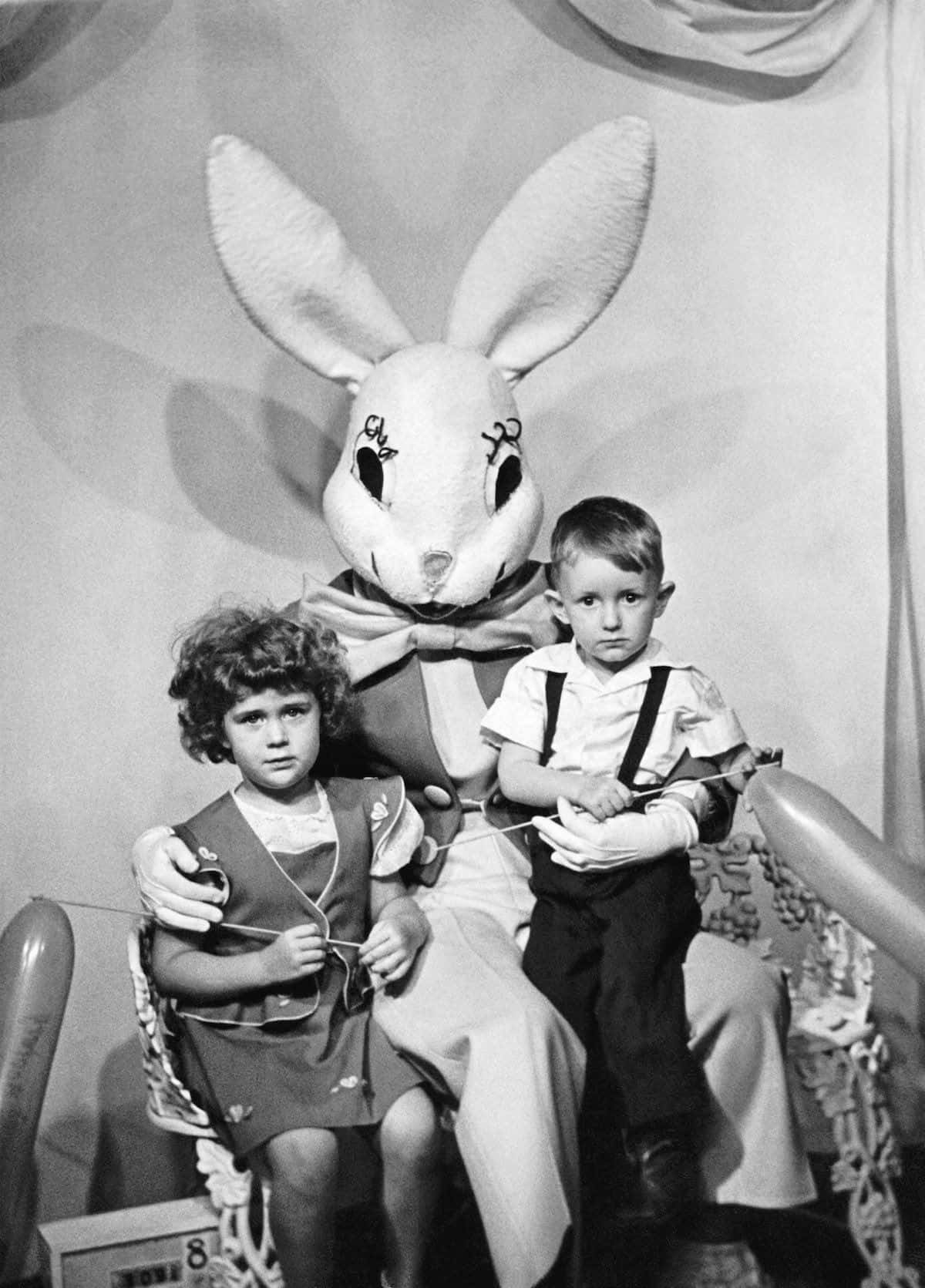 Creepy Easter Bunny 桌布 壁紙 — 一張復古黑白照片顯示兩個孩子坐在一個大型裝扮的復活節兔子旁邊，為工作室肖像擺姿勢。