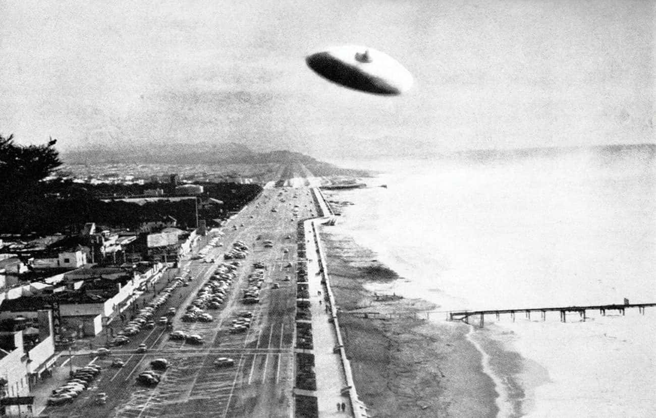 復古 桌布 壁紙 — 一張復古黑白照片顯示經典飛碟懸浮在沿海高速公路之上，下方有汽車和碼頭。