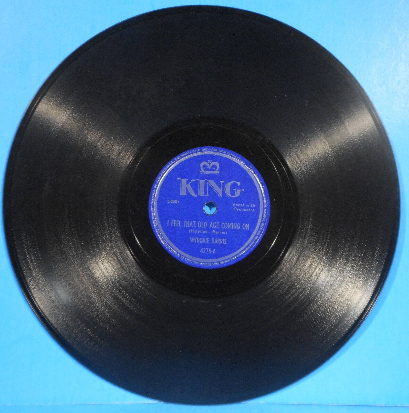 vinyl 桌布 壁紙 — 一張復古黑色黑膠唱片，帶有藍色King標籤，展示Wynonie Harris和歌曲I Feel That Old Age Coming On，置於純藍色背景上。