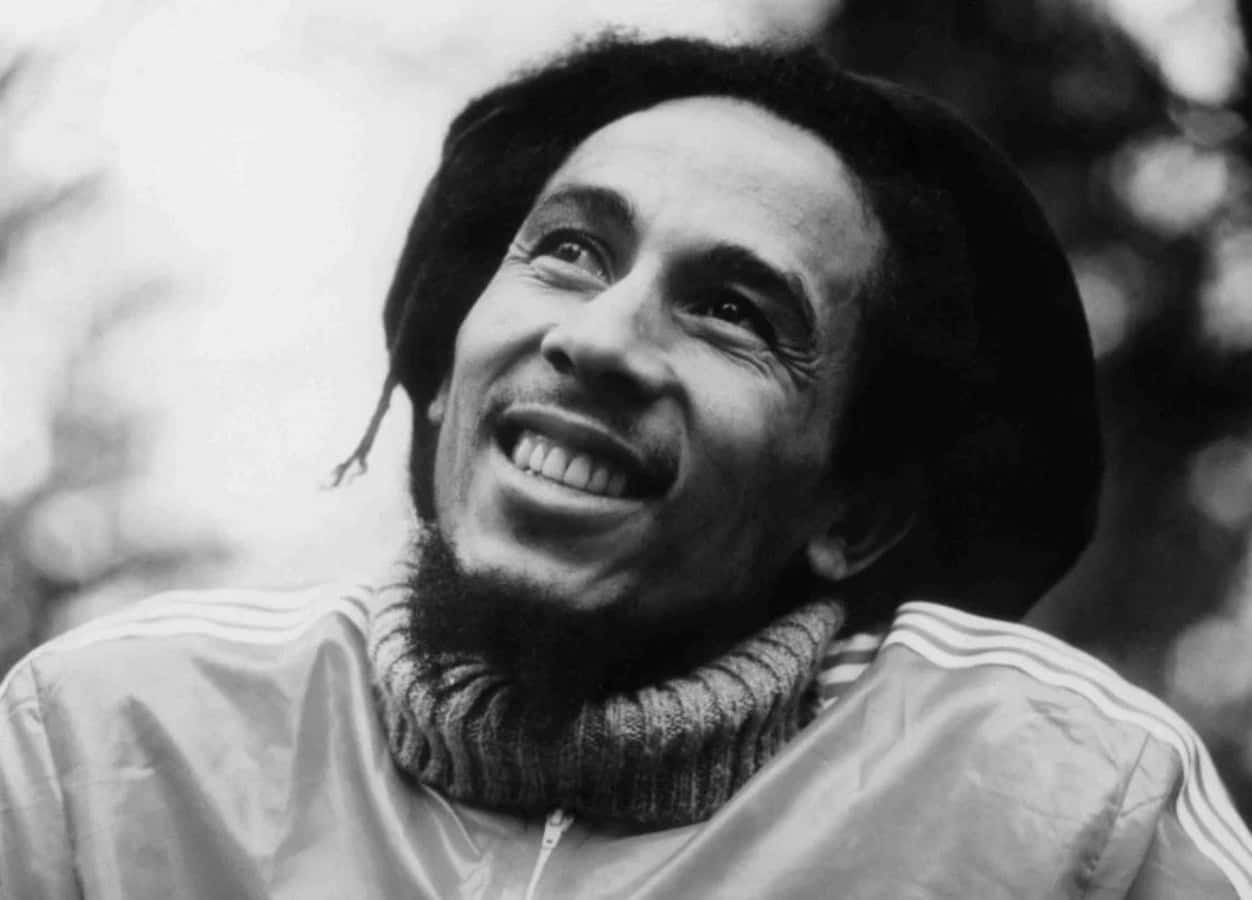 Bob Marley 桌布 壁紙 — 一張快樂的黑白肖像，Bob Marley 露出燦爛的笑容，帶有標誌性的辮子和 Adidas 外套。