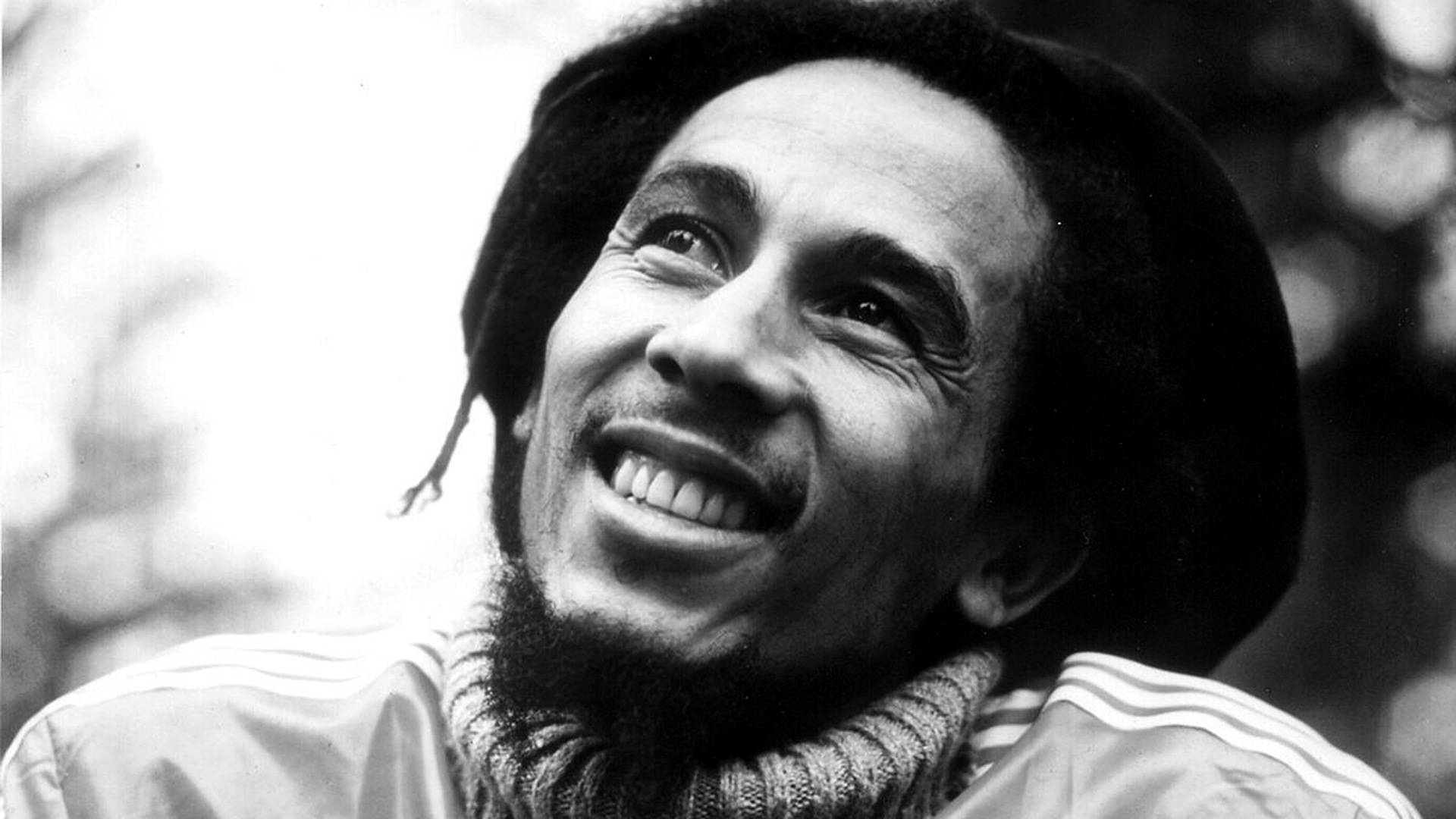 音樂 桌布 壁紙 — 一張快樂的黑白肖像，Bob Marley 向上微笑，帶有標誌性的辮子和 Adidas 外套。